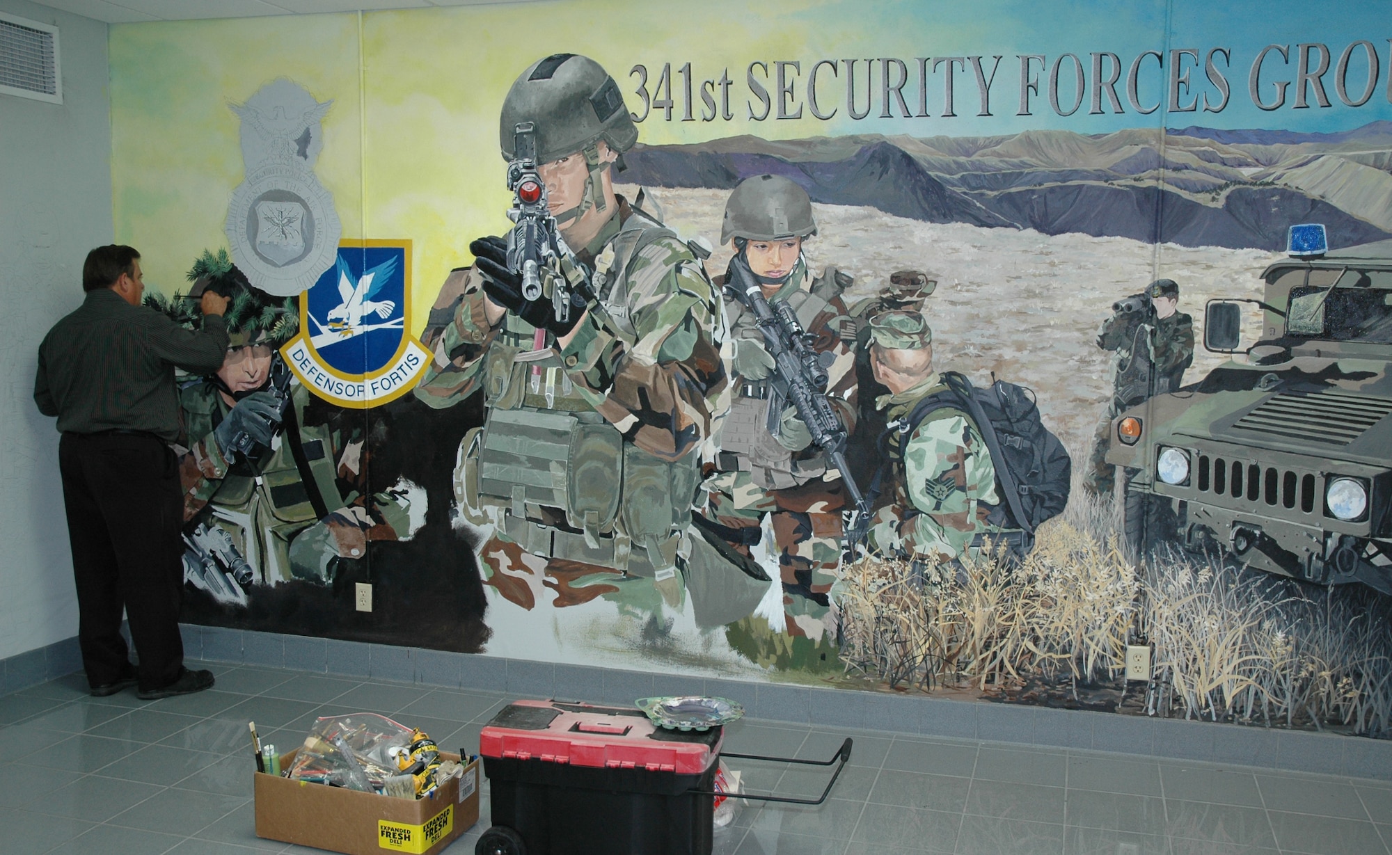 Bob Stillwell, 341st Communications Squadron graphic illustrator, adds detail to a tree branch on a mural in the headquarters building near the 341st Security Forces Group’s command suite at Malmstrom Air Force Base. The retired Air Force senior master sergeant received help from his son, Bob, and 11-year-old grandson, Logan. Mr. Stillwell has 182 hours of work into the mural and expects to have the mural completed in about 20 more hours. Bob’s son is planning to return in November so the duo can paint a mural of 341st Security Forces Group Tactical Response Force members on an adjacent wall. (U.S. Air Force photo/Airman 1st Class Dillon White)