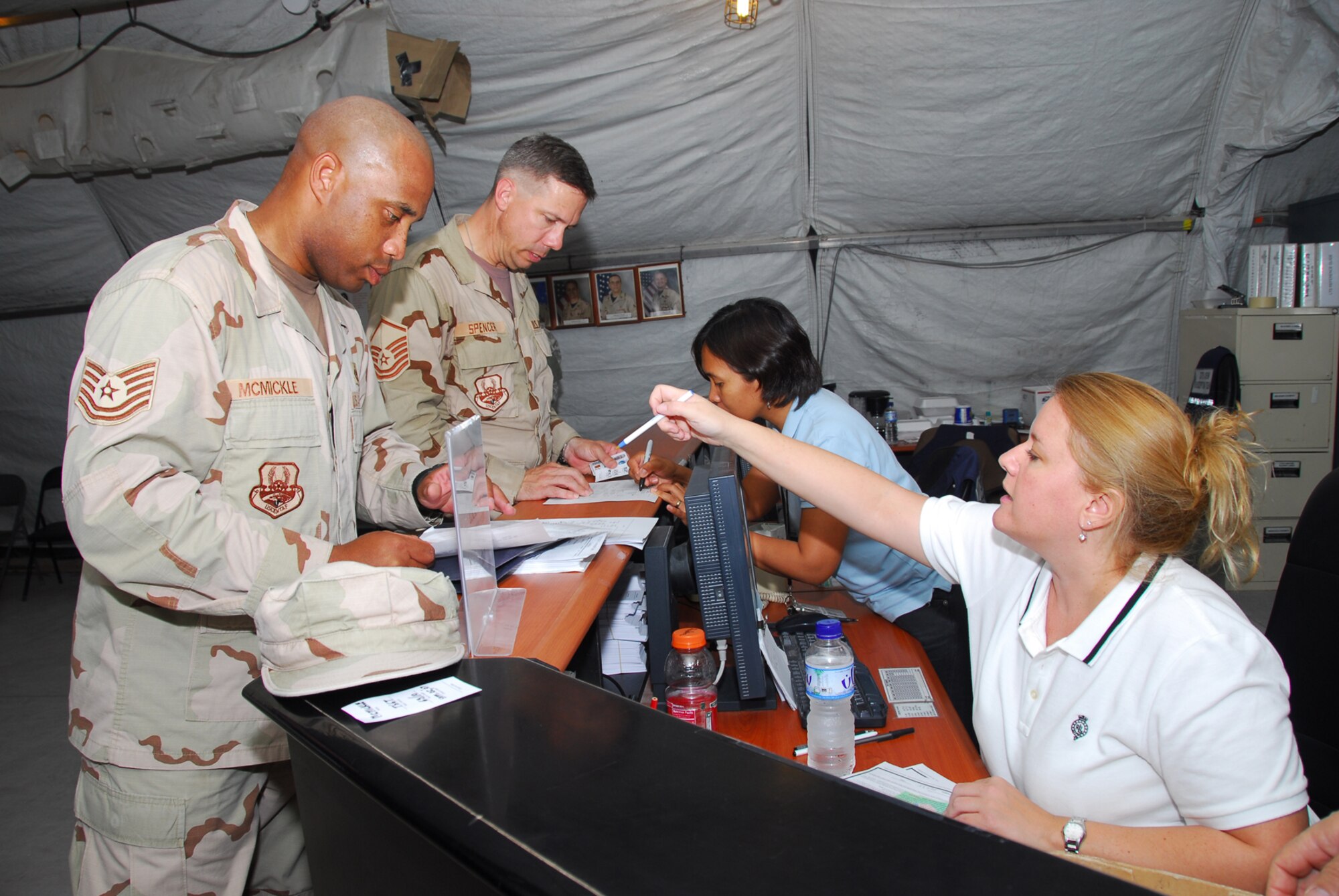 A member of the 379th Expeditionary Services Squadron (right), checks Tech. Sgt. Erskin McMickle (left) and Master Sgt. Michael Spencer (second from left) into temporary quarters while they wait for a connecting flight into theater. (U.S. Air Force photo by Airman 1st Class Ashley Tyler)