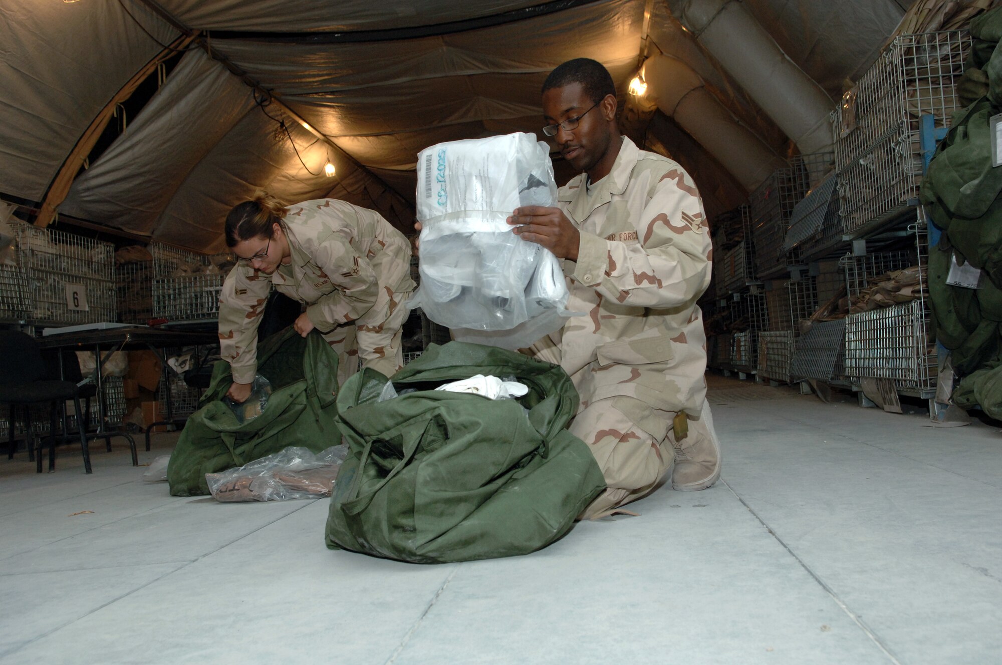 Two Airmen passing through the 379th Air Expeditionary Wing on their way to Iraq go through mobility bags issued to them at the Expeditionary Theater Deployment Center, ensuring all the equipment matches their inventory sheets. (U.S. Air Force photo by Master Sgt. Ken Stephens)