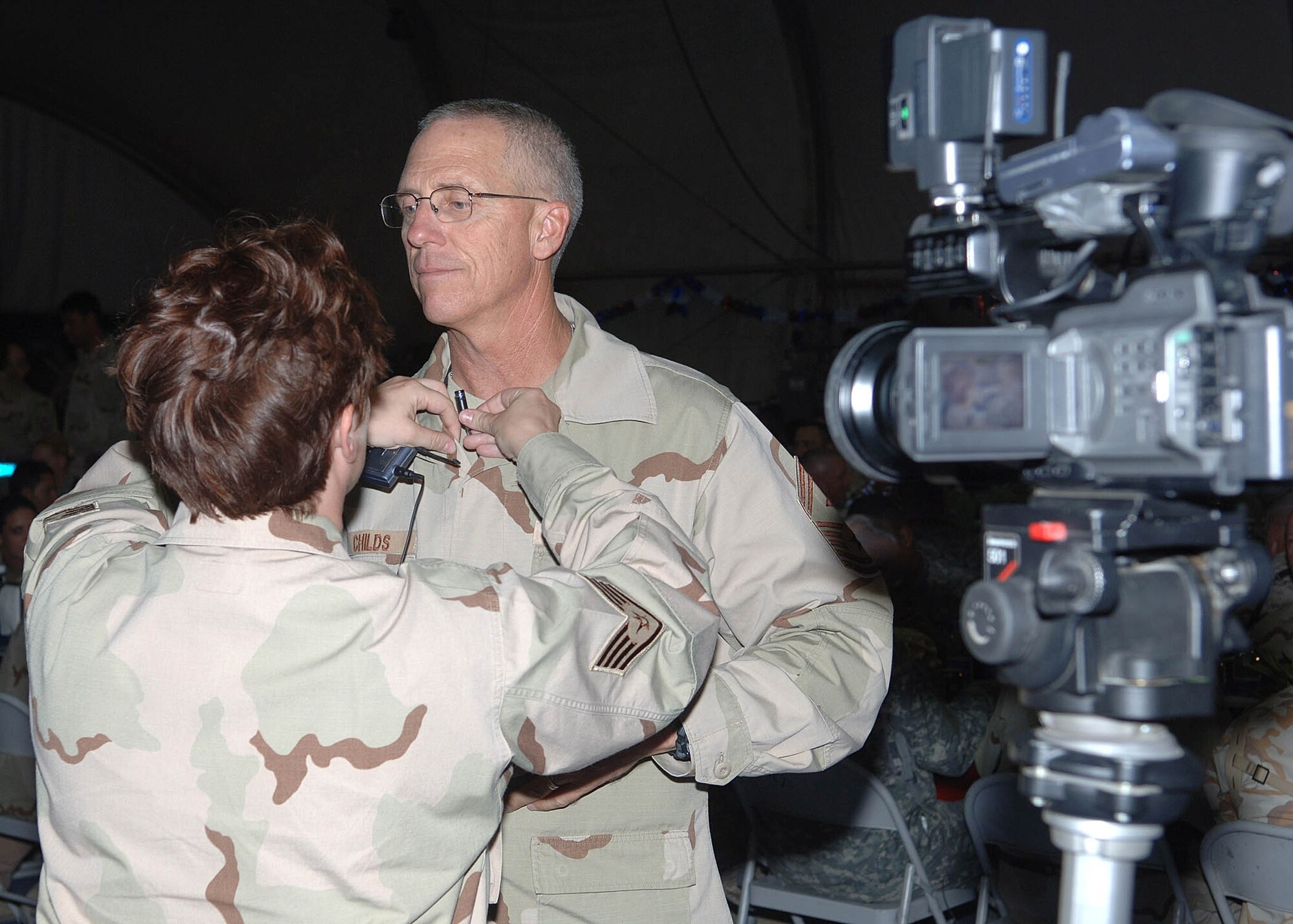 Staff Sgt. Stephanie Csornok (left mics up Senior Master Sgt. Ross Childs prior to filming an Air Force 60th Anniversary "Shout out" Sept. 8 at Bagram Air Base, Afghanistan. During the Air Force 60th Anniversary Ball, Airmen were invited to participate in video birthday messages to  send back to the United States. Sergeant Csornok is assigned to the Armed Forces Network Afghanistan, and Sergeant Childs is the 455th Expeditionary Mission Support Group first sergeant. (U.S. Air Force photo/by Staff Sgt. Craig Seals)