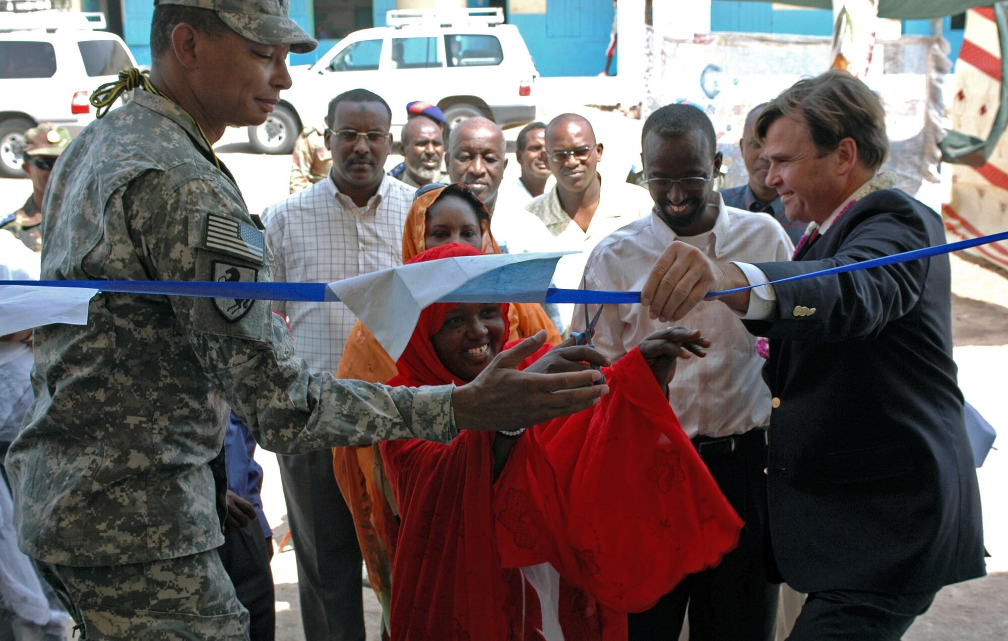 Army Brig. Gen. Sanford Holman and Stuart Symington assist a local teacher in cutting a ribbon at the dedication  ceremony Sept. 6 for the of new classrooms, stocked library, bathroom facilities, stage area and power supply to the Goubetto primary school in the village of Balbala. The ceremony highlighted the hand-over of the facility to the local community to take care of and preserve. General Holman is the Combined Joint Task Force-Horn of Africa deputy commander and Mr. Symington is the U.S. Ambassador to Djibouti. (U.S. Army photo/Army Sgt. Brandon McCarty)
