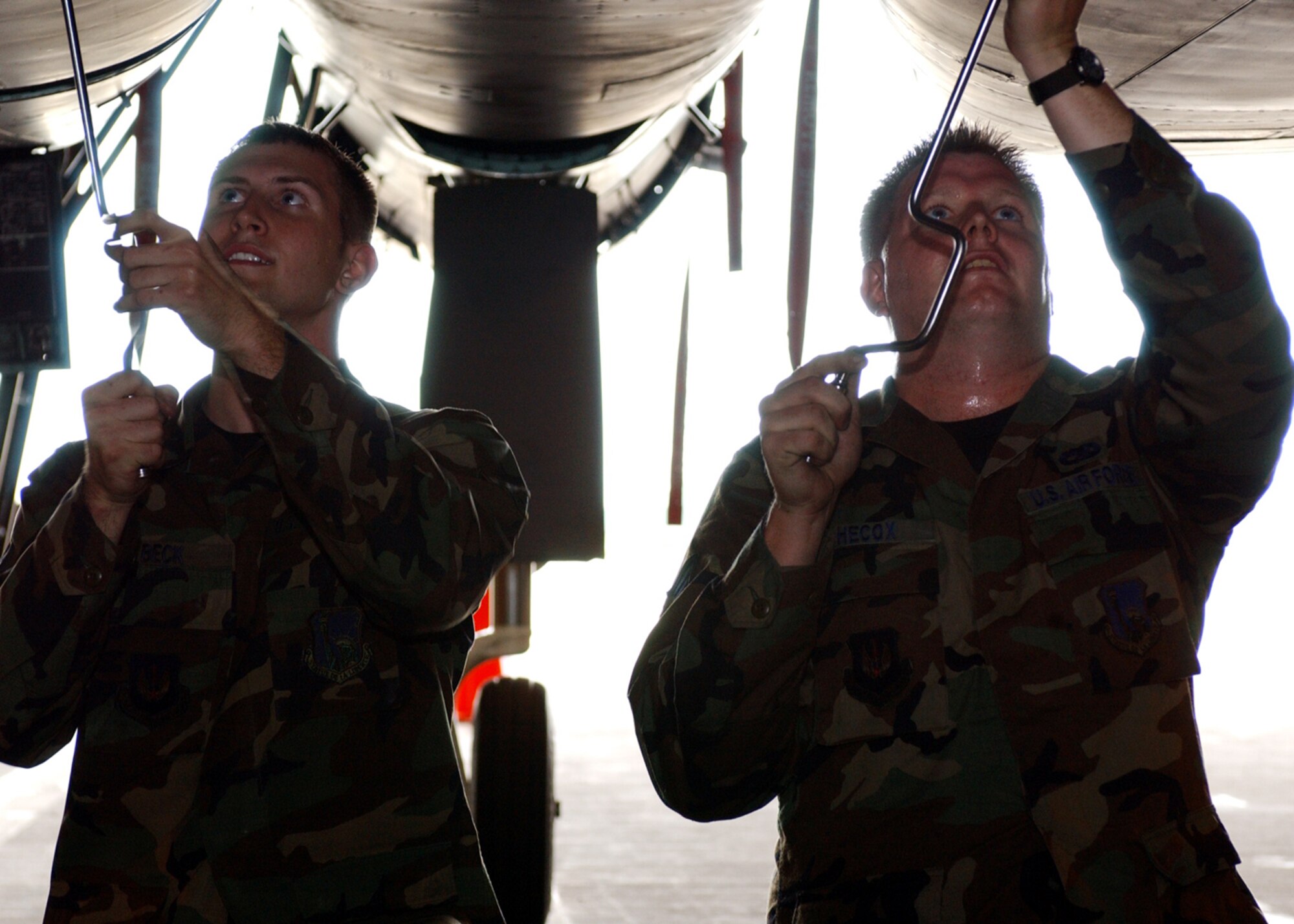 Left to right, Senior Airman Kyle Beck and Staff Sgt. Andrew Hecox, 48th Aircraft Maintenance Squadron, crew chiefs, work simultaneously to unscrew paneling underneath an F-15 Eagle for repairs. (U.S. Air Force photo by Airman 1st Class Torri Ingalsbe)