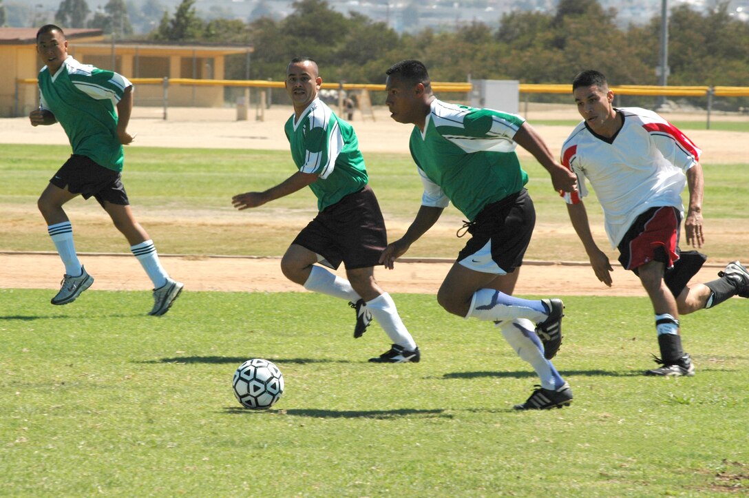 Support Bn.?s Staff Sgt. Jose Umana, Staff Sgt. Enrique Mayorga and Gunnery Sgt. Christopher Niemas take the ball in to 12th MCD territory to score a goal as Sgt. Nicholas Lopez attempts to stop them.