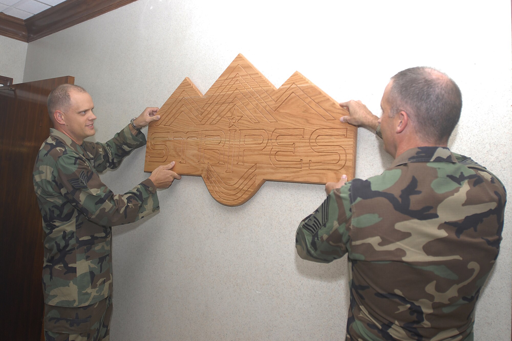 Staff Sgt. Jeffrey Fitzmorris (left), 21st Mission Support Squadron, and Chief Master Sgt. Tim Omdal, 21st Space Wing chief, hang the sign to the new Stripes Pub Sept. 6. Sergeant Fitzmorris designed the logo for the Pub, located at The Club. (U.S. Air Force photo)