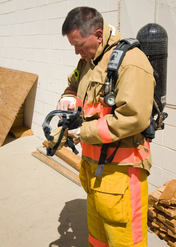 Col. Bryan Gallagher, 95th Air Base Wing commander, inspects his mask during the Edwards fire departments' training Monday. The training provided commanders with various fire fighting experience in the base's interior structural fire trainer. Base fire fighters use this training to maintain their proficiency and skills in fighting a structural fire. (Photo by Mike Cassidy)