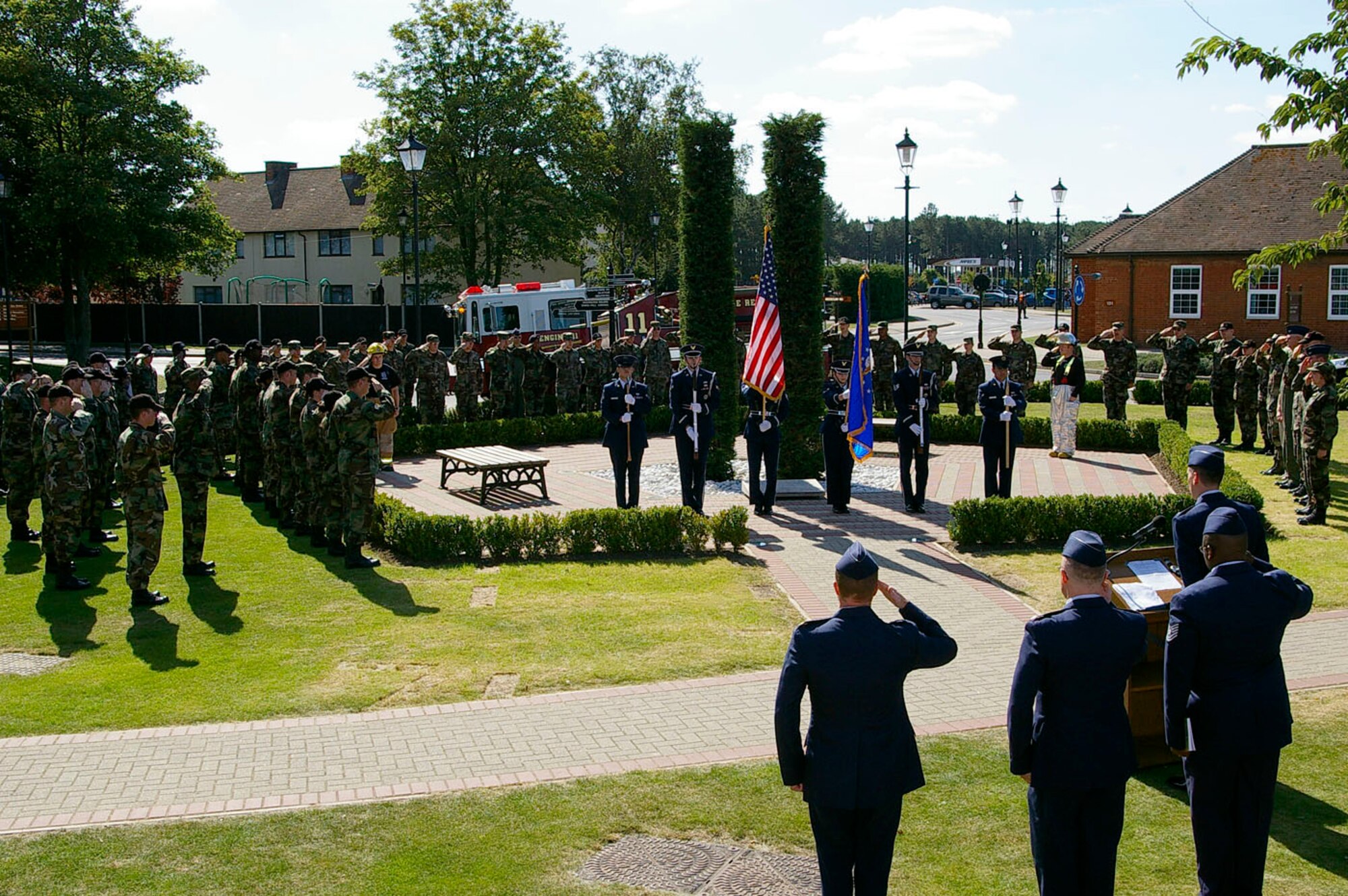 The base Honor Guard, Sub-Officer John Miller and Senior Airman Marcus Ring, both 100th Civil Engineer Squadron Fire Department, stand to attention within the pentagon area of Remembrance Park at the memorial service Sept. 11, as Team Mildenhall members also stand at attention, during the playing of the British national anthem. (U.S. Air Force photo by Karen Abeyasekere)