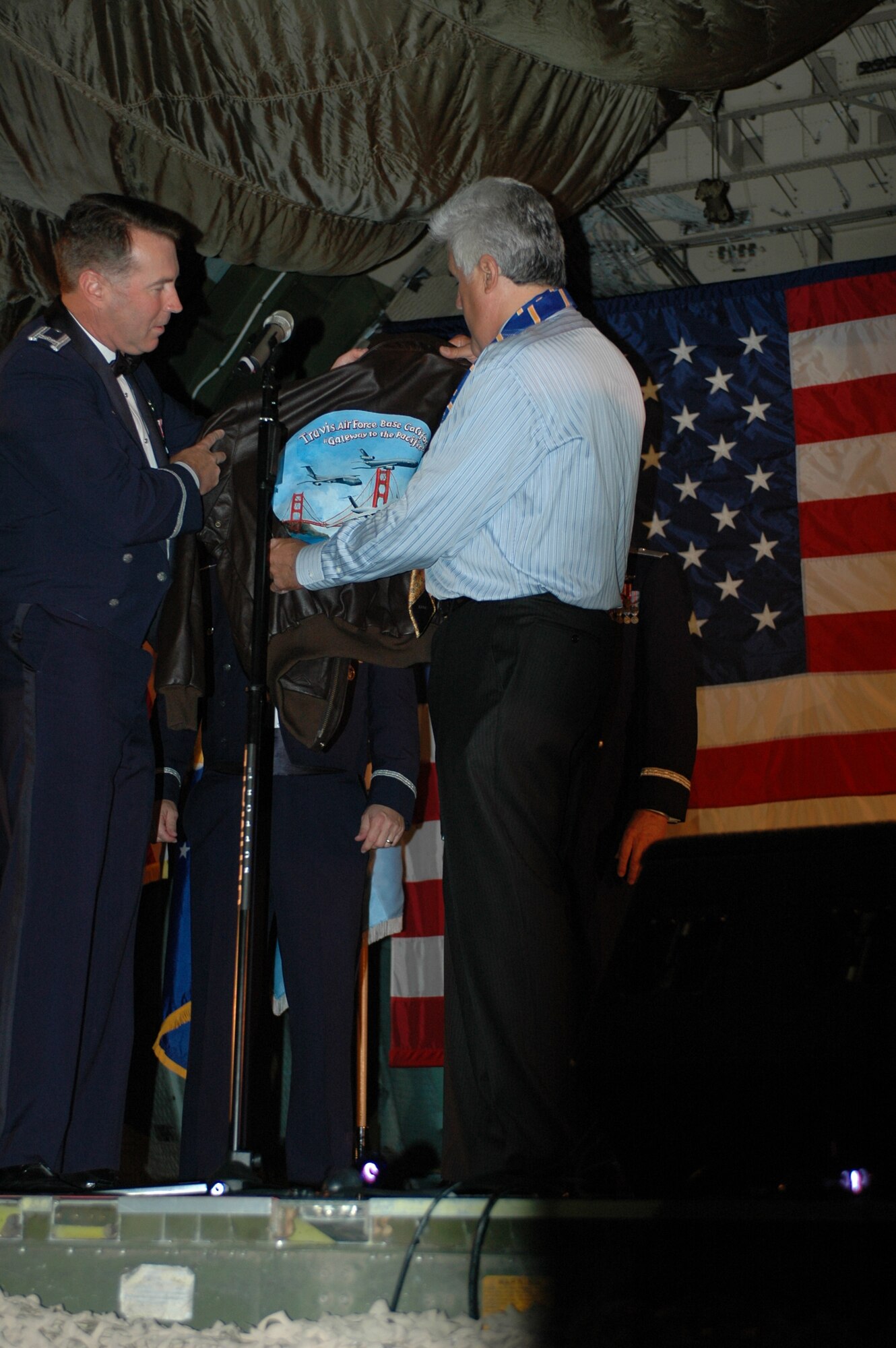 Col. Steve Arquiette, 60th Air Mobility Wing commander, presents Mr. Jay Leno with a leather flight jacket that reads, “Travis Air Force Base California, gateway to the Pacific.” (U.S. Air Force photo/Tech. Sgt. Donald Osborn)
