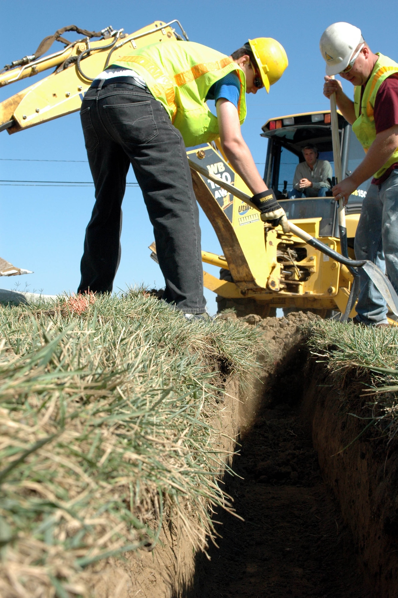 Spencer Low, (left), Russ Gentry, (backhoe driver), and Dan Postak, Gentry Construction, dig a trench to install a drainage system near playground equipment at the Duck Pond Sept.13. The parking area will remain open through all phases of the project. (U.S. Air Force photo/Staff Sgt Matthew McGovern)