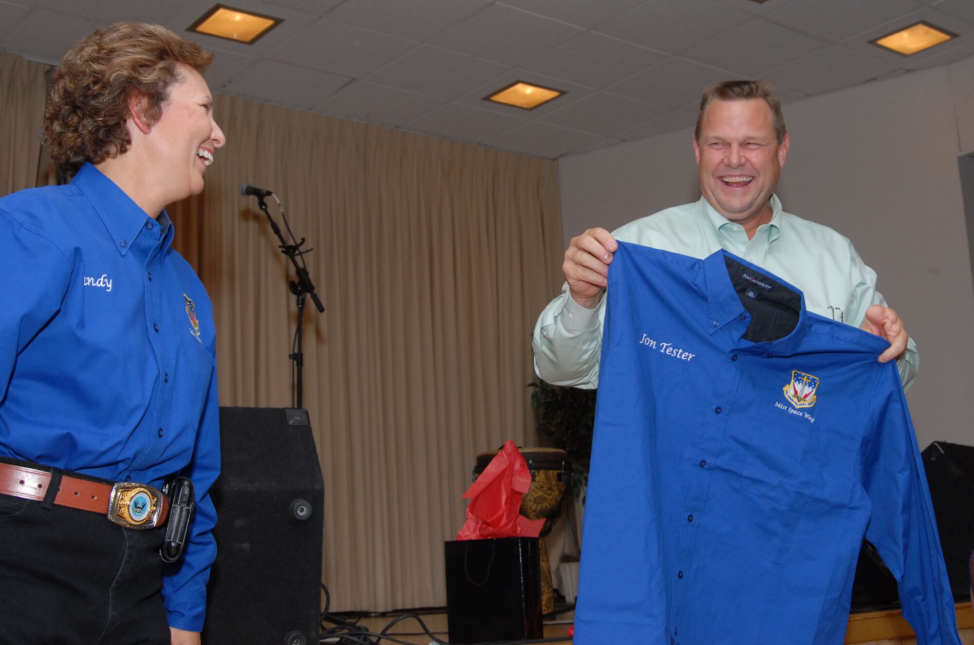 Col. Sandy Finan, 341st Space Wing commander, and Montana Senator Jon Tester share a laugh after she presented him with an honorary 341st Space Wing shirt. The gift was to thank him for being the guest speaker at the annual Salute to the Community Dinner at Malmstrom Air Force Base, Mont., Sept. 14. (U.S. Air Force photo/John Turner)