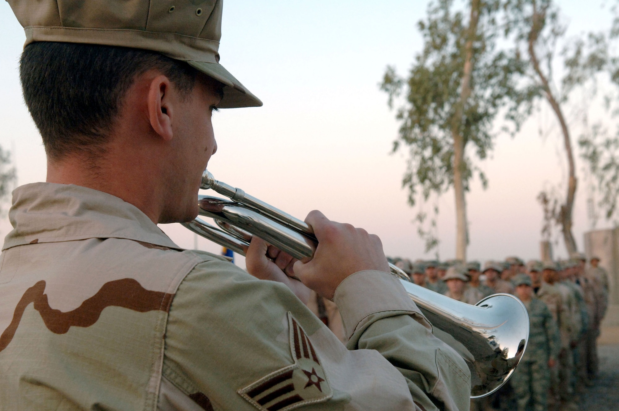 Members of the 332nd Air Expeditionary Wing stand at attention as Senior Airman Darren Ruch plays "Reveille" Sept. 18 at Balad Air Base, Iraq. Members of the 332nd AEW, the most forward-deployed Air Force wing in Iraq, held the ceremony in observance of the Air Force's 60th birthday. The wing draws its heritage from the famed 332nd Fighter Group, led by the Tuskegee Airmen of World War II, and carries this spirit in operations here. Airman Ruch is assigned to the 332nd Expeditionary Operations Support Squadron. (U.S. Air Force photo/Staff Sgt. Joshua Garcia) 
