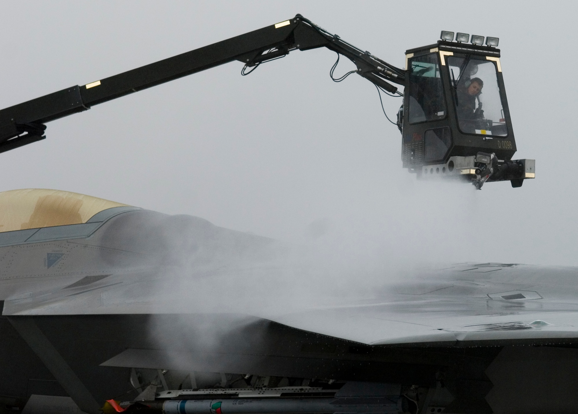 ELMENDORF AIR FORCE BASE, Alaska -- Airman 1st Class Alexander Buck, 3rd Aircraft Maintenance Squadron, de-ices an F-22A Raptor . The de-icing test will help officials gather technical data on how cold weather effects the maintenance crew's capabilities while working with this aircraft during the winter. The onset of termination dust on the surrounding mountain ranges is a sign the Alaskan winter is just around the corner. (U.S. Air Force Photo by Senior Airman Garrett Hothan)