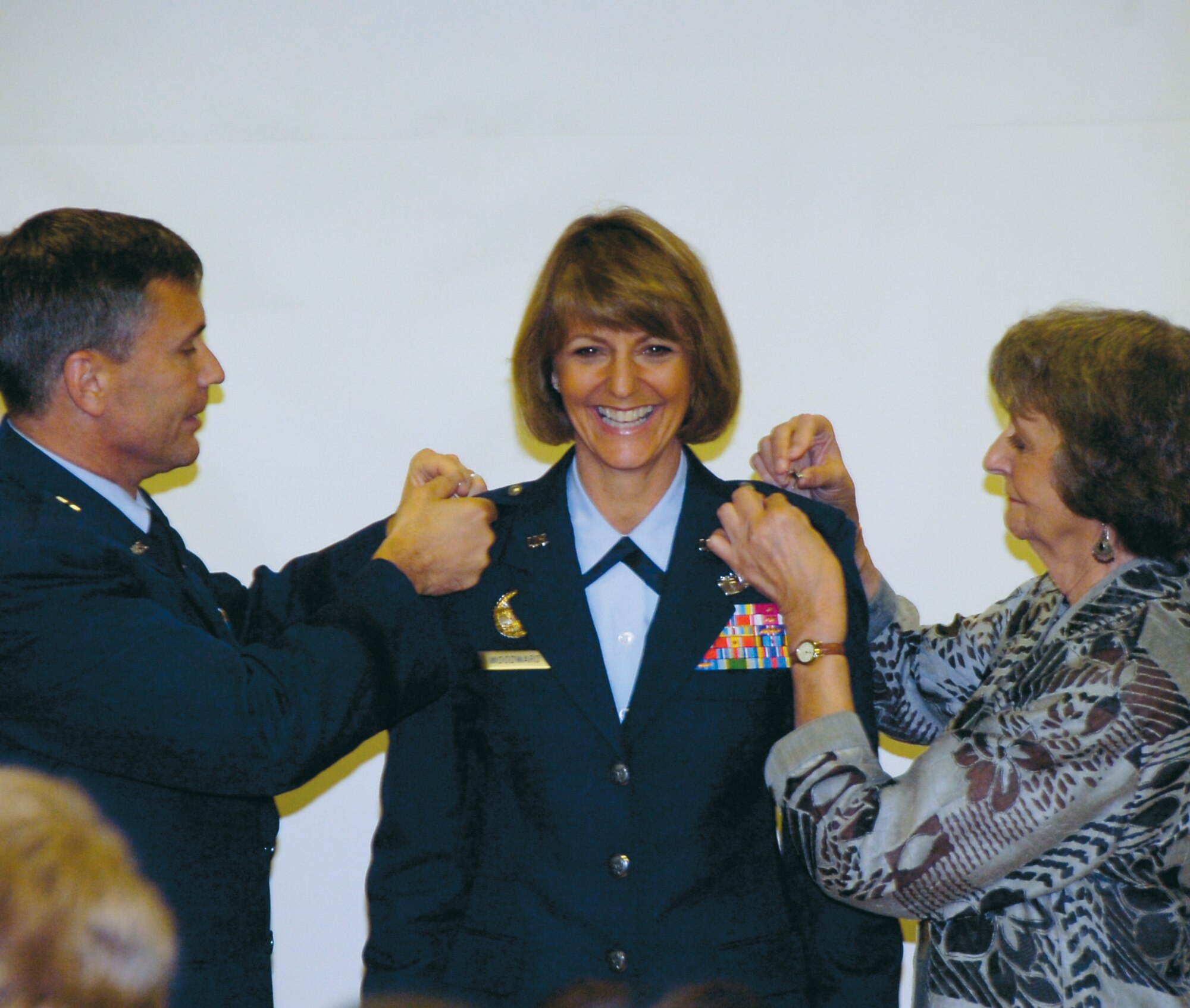 Brig. Gen. Maragaret Woodward, 89th Airlift Wing commander stands at attention as her husband, Brig. Gen. Daniel P. Woodward and mother Mary Ann Maslowski remove her eagles, representing the rank of Colonel, and pin on single stars representing the rank of Brigadier General. (US Air Force/Bobby Jones)