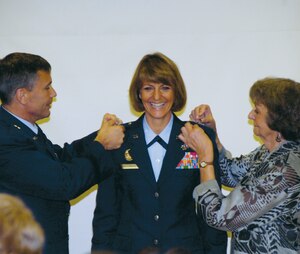 Brig. Gen. Maragaret Woodward, 89th Airlift Wing commander stands at attention as her husband, Brig. Gen. Daniel P. Woodward and mother Mary Ann Maslowski remove her eagles, representing the rank of Colonel, and pin on single stars representing the rank of Brigadier General. (US Air Force/Bobby Jones)