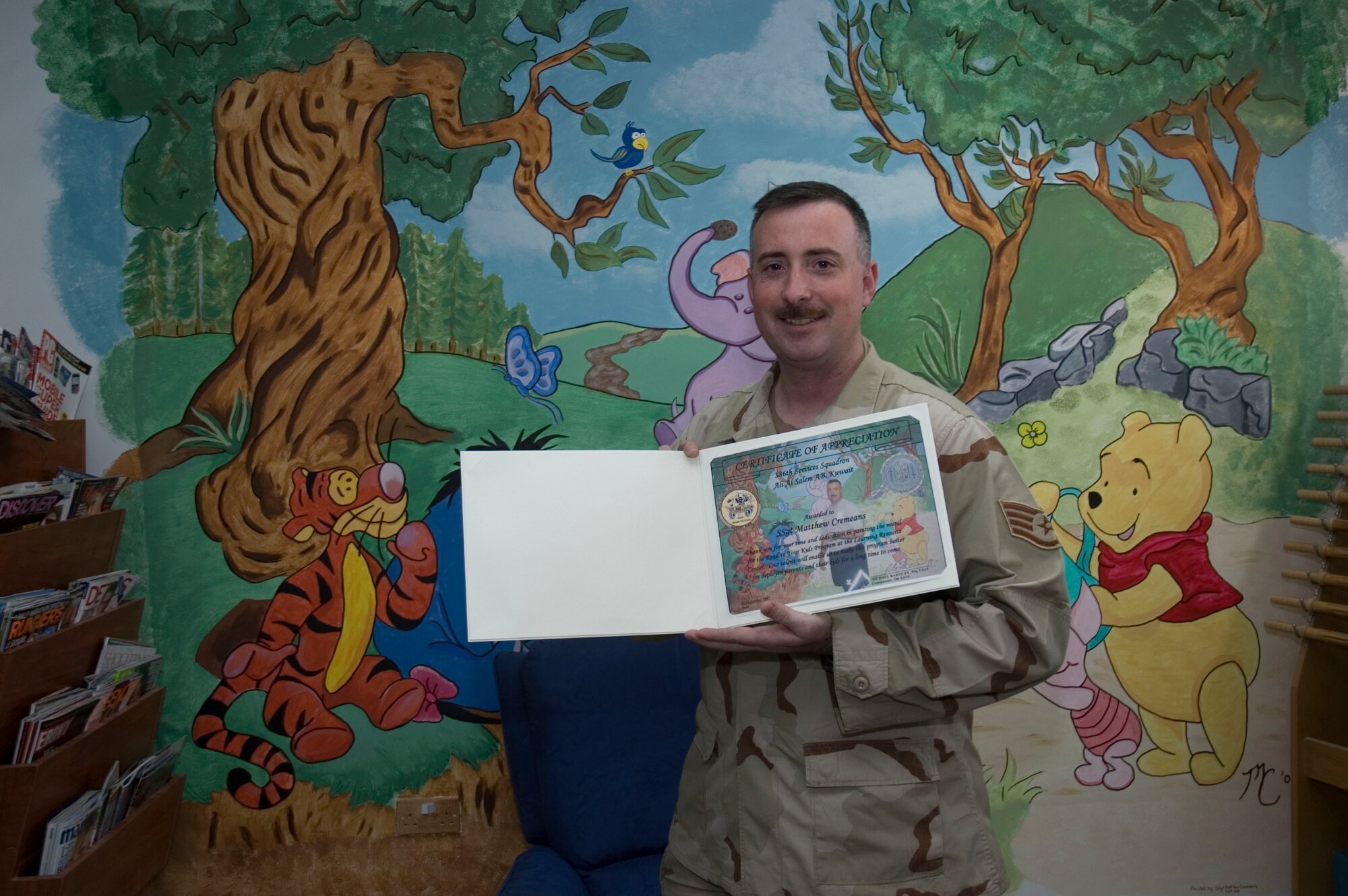 SOUTHWEST ASIA -- Staff Sgt. Matthew Cremeans, 386th Expeditionary Wing, consolidated tool crib NCO in charge receives a certificate of appreciation Sept 15 for a mural he painted at the Learning Resource Center.  The mural depicting Winnie the Pooh and friends took over 40 hours to complete.  (U.S. Air Force photo by Staff Sgt. Tia Schroeder)