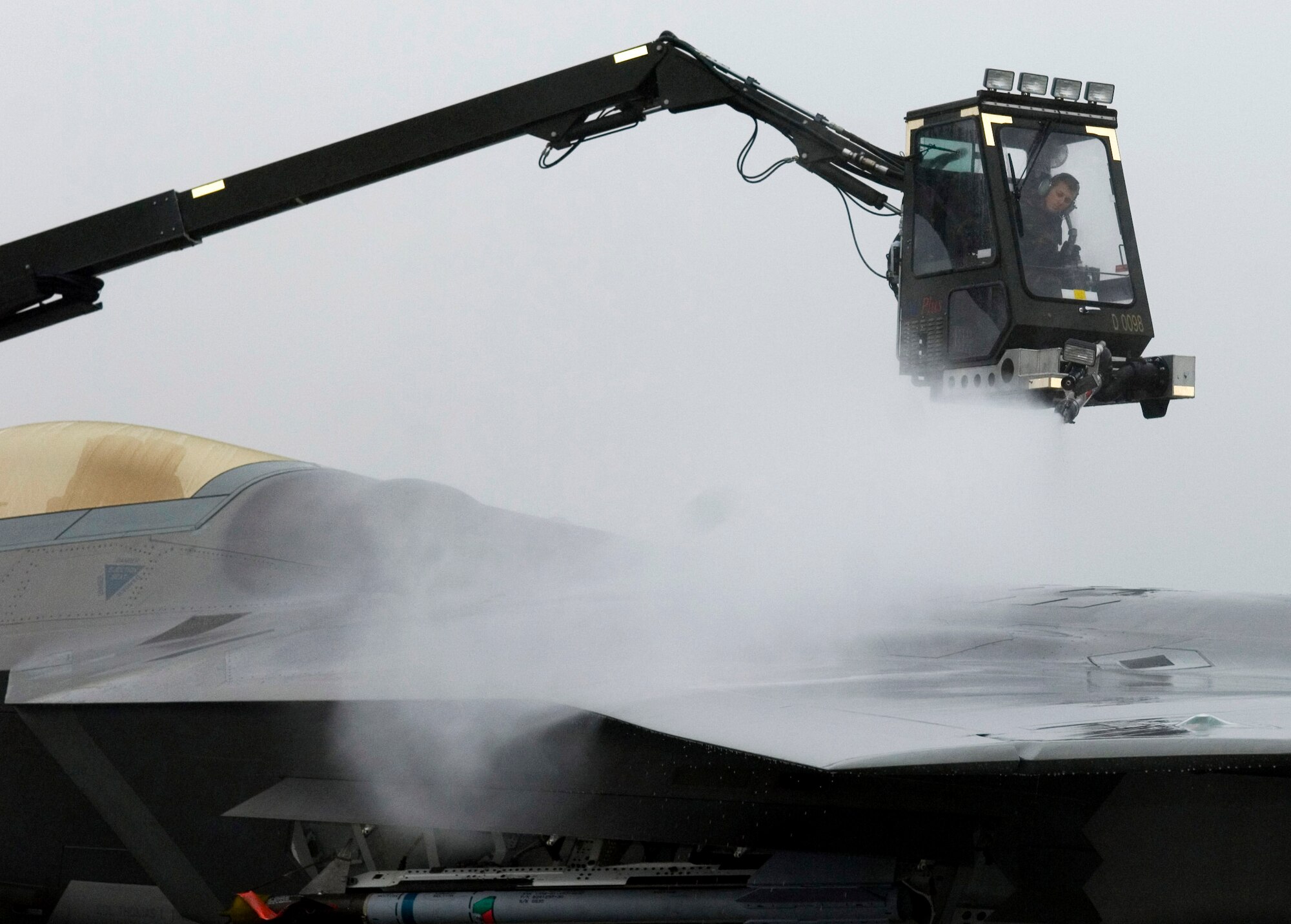 Airman 1st Class Alexander Buck practices de-icing an F-22 Raptor Sept. 19 at Elmendorf Air Force Base, Alaska. The de-icing test will help officials gather technical data on how cold weather effects the maintenance crew's capabilities while working with this aircraft during the winter. The onset of light dustings of snow on the surrounding mountain ranges is a sign the Alaskan winter is just around the corner.  Airman Buck is assigned to the 3rd Aircraft Maintenance Squadron.  (U.S. Air Force photo/Senior Airman Garrett Hothan)