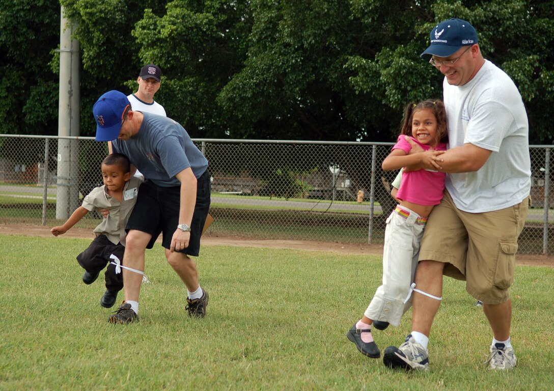 SOTO CANO AIR BASE, Honduras -- Air Force Tech. Sgt. David Johnson (front), airfield management, assists his Honduran partner in a three-legged race against Capt. Michael Epper, 612th Air Base Squadron, and his younger counterpart.  Approximately 90 children from Nuestra Señora de Guadalupe Children's Home in Comayagua came out to enjoy the Annual Kids Day celebration September 22.  (U.S. Air Force photo by Staff Sgt. Austin M. May)