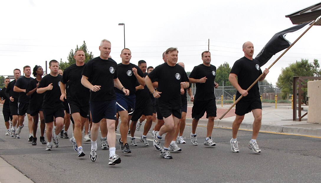 A formation of 5th Annual POW/MIA 24-Hour Vigil Runners from Kirtland AFB, N.M., led by Maj. Gen. Stephen T. Sargeant, Air Force Operational Test and Evaluation Center Commander (front middle) and Col. Matthew Bartlett, AFOTEC Vice Commander (front left), carry the POW/MIA flag from Kirtland's Hardin Field along a 1.5 mile course at the culmination of the run to deliver the flag to the off-base New Mexico Veterans Memorial on Sept. 21 for the combined POW/MIA Recognition Day ceremony sponsored by the Kirtland and Albuquerque communities.