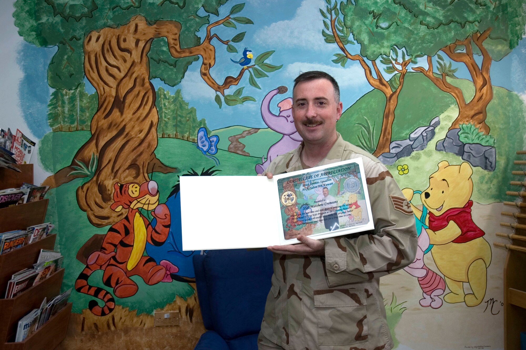 Staff Sgt. Matthew Cremeans holds a certificate of appreciation he received Sept 15 for the mural he painted at the Learning Resource Center at his deployed location in Southwest Asia. The mural, depicting Winnie the Pooh and friends, took over 40 hours to complete.  Sergeant Cremeans is the 386th Air Expeditionary Wing consolidated toll kit NCO in charge. (U.S. Air Force photo/Staff Sgt. Tia Schroeder)