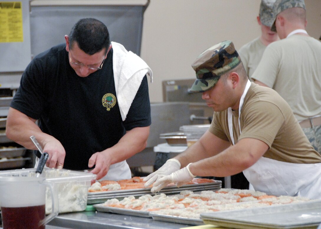Staff Sgt. Mario Frank (right) spreads a paste on salmon Sept. 22 as the Food Network's Chef Robert Irvine prepares salmon on another tray for the 60th Anniversary celebration of the Air Force that evening at Sheppard. Chef Robert and a film crew from the 'Dinner: Impossible' accepted a mission that same morning to prepare 1,000 meals for Airmen and guests in Hangar 1045. (U.S. Air Force photo/Harry Tonemah)