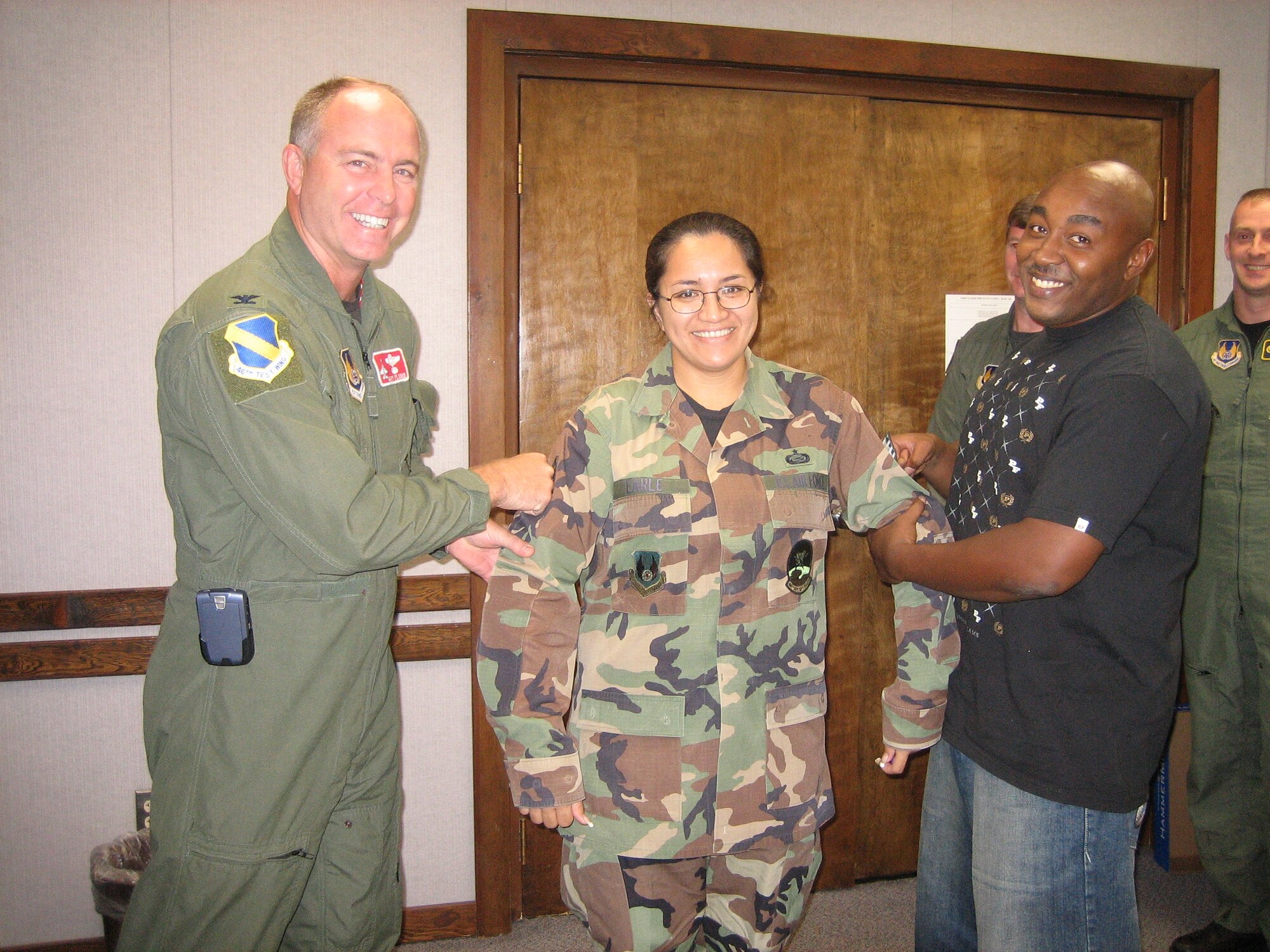 (Center) Tech. Sgt. Malia Earle, 46th Operations Group Training Manager, gets new stripes pinned on by (left) Col. Gary Plumb, 46th Test Wing Commander, and her husband (right), Tech. Sgt. Freddrick Earle, 96th Logisitics Readiness Squadron in a Stripes for Exceptional Performers program.