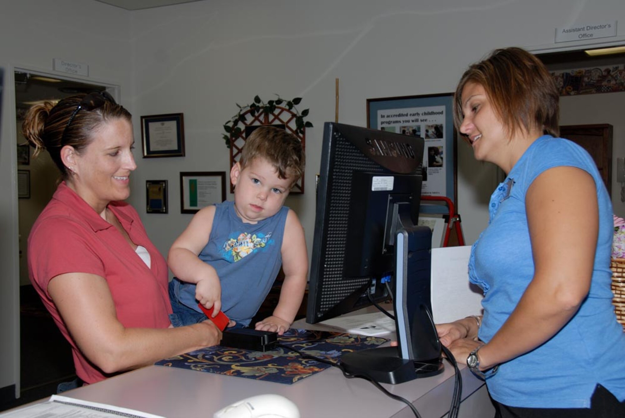 MISAWA AIR BASE, Japan -- Ann Leach (right) and her son Mason swipe an identification card at the child development center here as Theresa Goodwin, CDC desk clerk, monitors the front desk. The ID cards are used to check the children in and out of the center. (U.S. Air Force photo by Senior Airman Laura R. McFarlane)