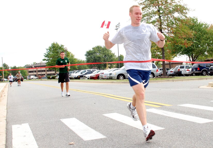 Capt. Dan Pearson, 844th Communications Group, crosses the finish line waving a miniature flag during the Hispanic Heritage Fun Run held at the West Fitness Center Sept 14. Captain Pearson came in 1st place with a run time of 20 minutes 8 seconds.