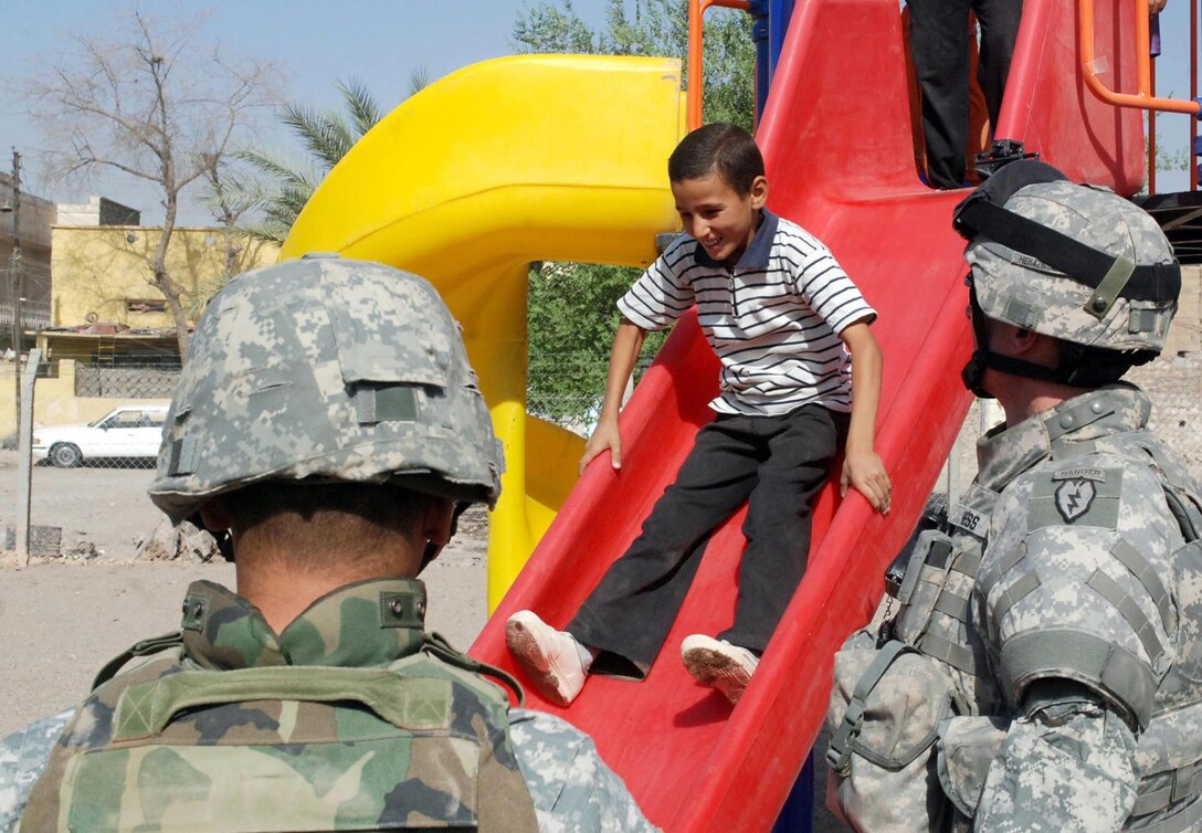 U.S. Army Lt. Col. James D. Hess (right), commander, 325th Brigade Support Battalion, 3rd Infantry Brigade Combat Team, watches a young Iraqi boy enjoy one of four large slides during the grand opening of the Tisin Playground in Kirkuk, Iraq, Sept. 24, 2007.
