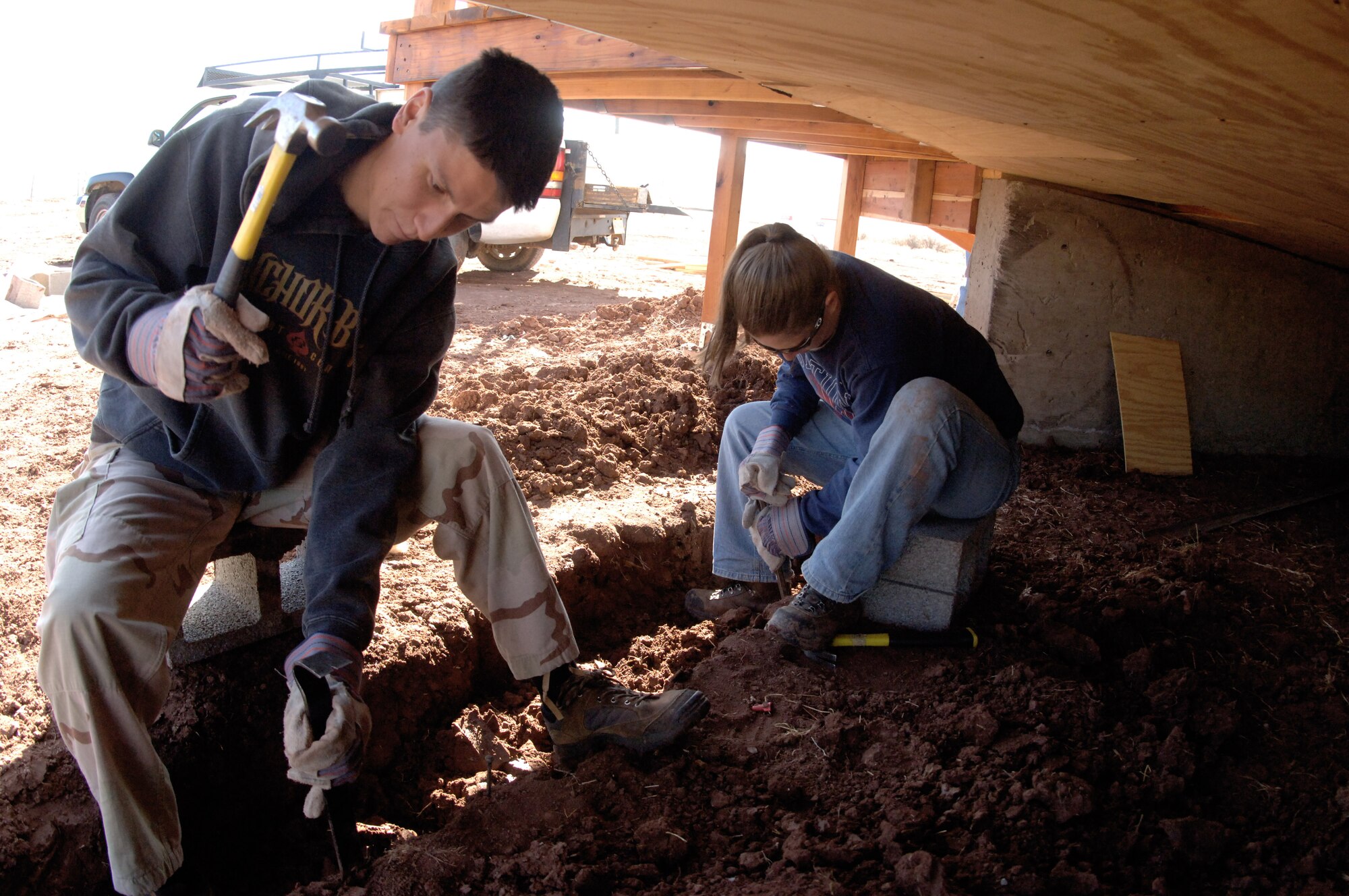 Air Force Academy Cadet 3rd Class Ted Ornelas and Cadet 2nd Class Holly Bigelow excavate frozen soil from underneath an Academy-built Navajo Hogan March 26 in Navajo, N.M. The soil must be excavated before concrete and block can be set to finish the traditional eight-sided Navajo home's foundation. The hogan will provide a home for a family on the Navajo reservation in northwest New Mexico. Cadets Bigelow and Ornelas are part of a group of 20 cadets, civil engineering faculty and family members who volunteered during the Academy's spring break to work on the Navajo reservation. (U.S. Air Force photo/John Van Winkle)