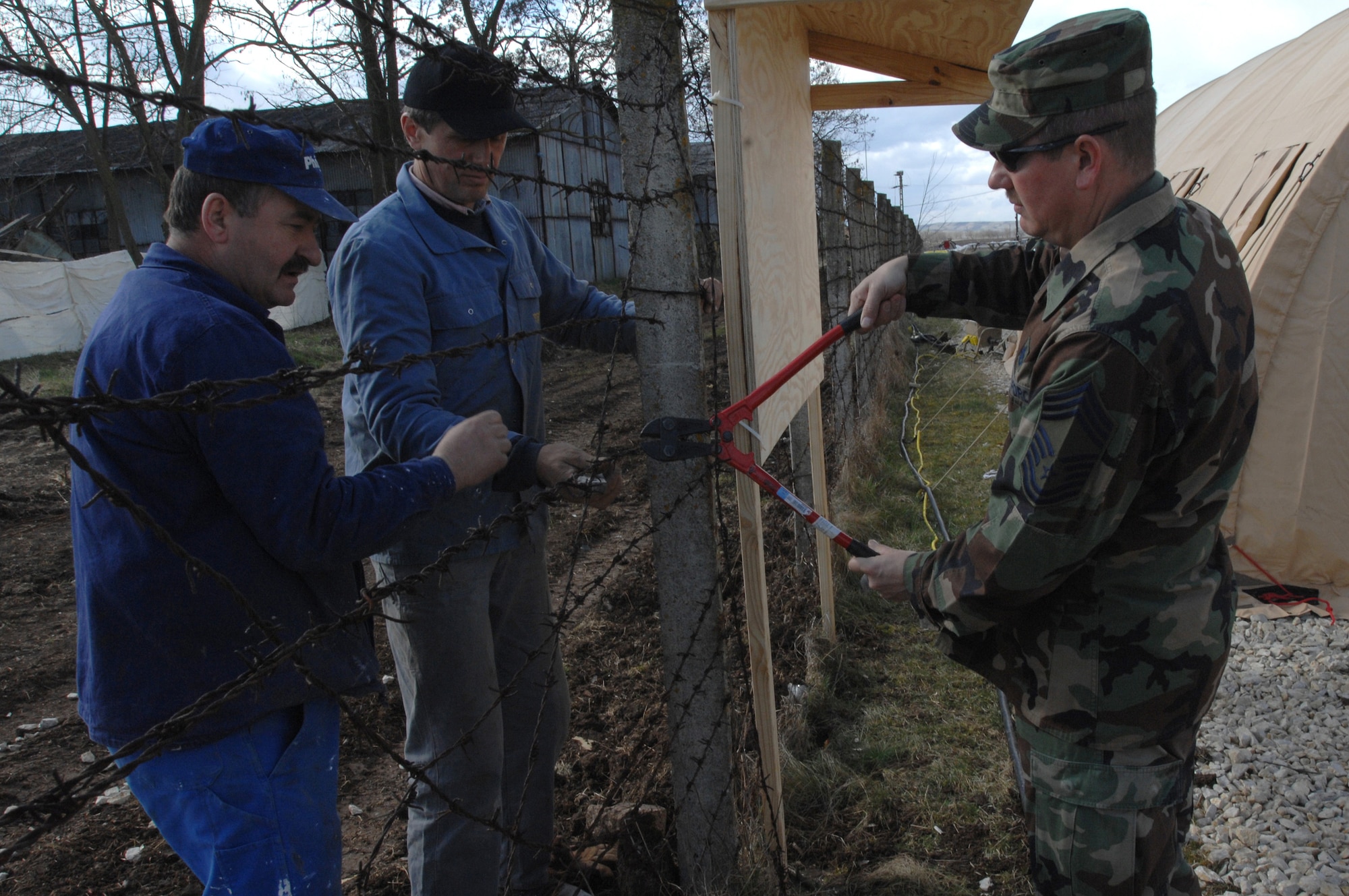 CAMPIA TURZII, Romania -- Chief Master Sgt. Terry Masters, chief of the 404 Expdentionary Air Base Squadron works with Romanian nationals in cutting the fence bewteen the Romanian base and tent city here March 24, 2008. The deployed civil engineering team built an entire tent city here in 96 hours to support U.S. operations at the air base.  The Airmen are part of a team which is augmenting NATO forces in securing the airspace around Bucharest, Romania, for the NATO Summit April 2-4,  (U.S Air Force photo by Senior Airman Teresa M. Hawkins)
