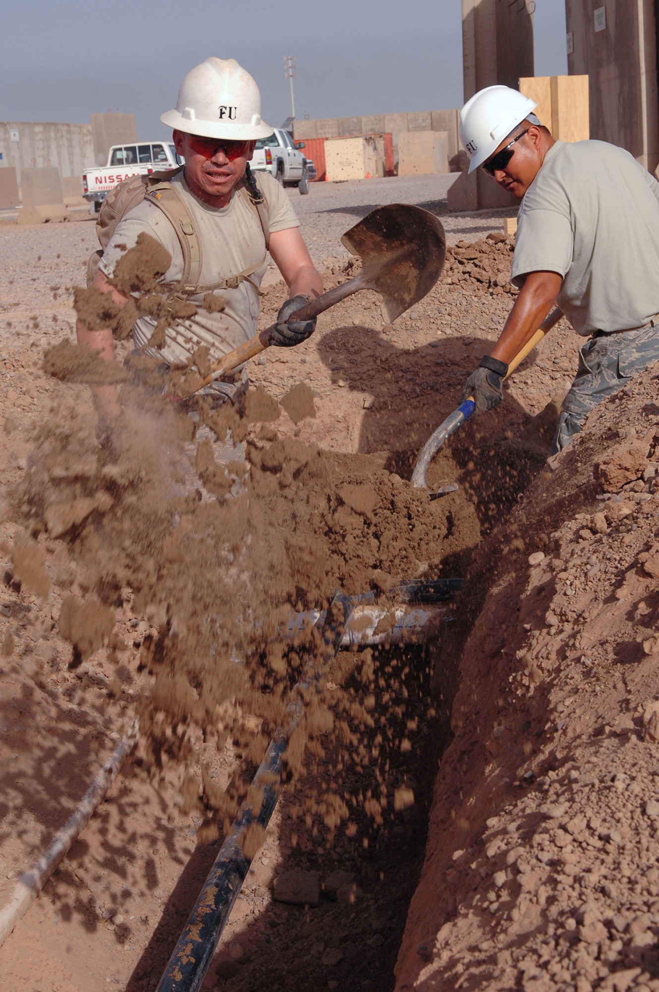 Senior Airmen Antonio Martinez and Juan Reynoso shovel soft sand over new piping March 24 at Balad Air Base, Iraq. The sand will protect and cushion the newly installed pipes in the Air Force housing area from rocks. The pipe infrastructure replacement project is scheduled to be completed by mid-June. Both Airmen are 332nd Civil Engineer Squadron fuels and utilities plumbers deployed from Peterson Air Force Base, Colo. (U.S. Air Force photo/Senior Airman Julianne Showalter) 
