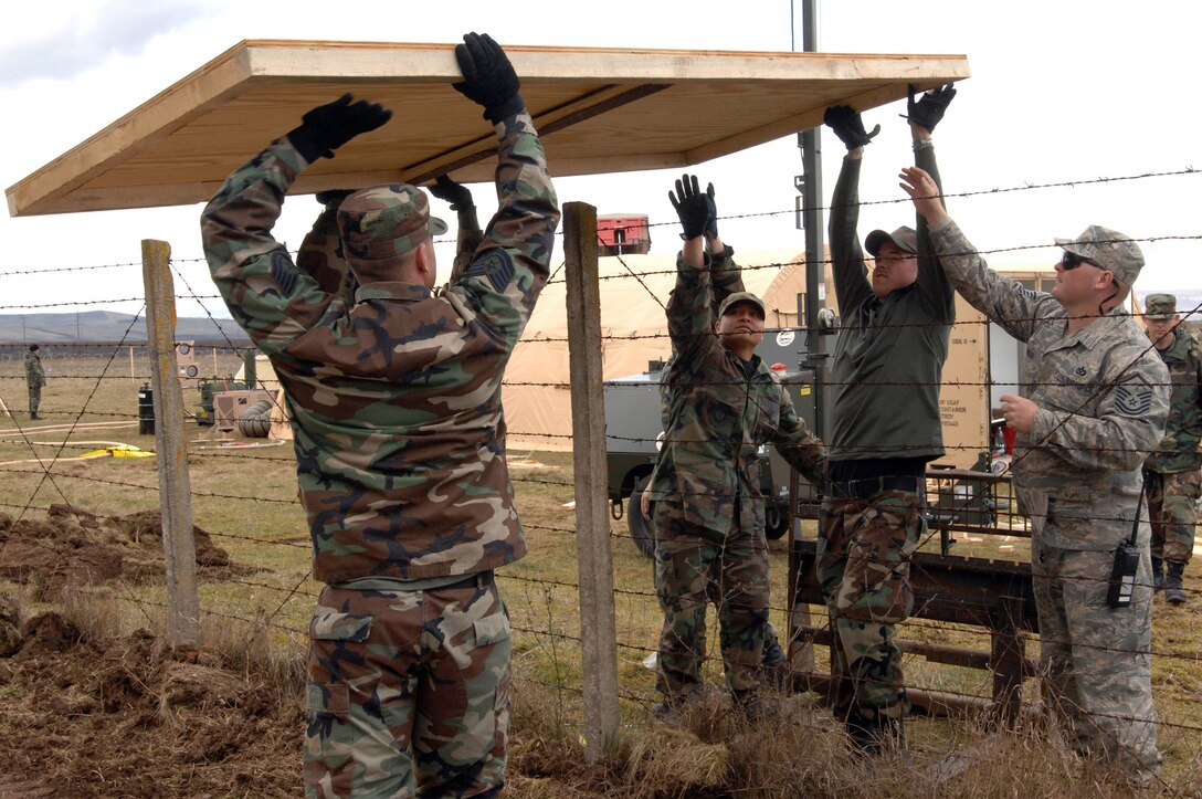 Members of the 404th Expeditionary Air Base Squadron pass a section of plywood flooring over a fence March 24 at the tent city on Campia Turzii, in Romania. The deployed civil engineering team built an entire tent city in 96 hours to support U.S. operations at the air base. The Airmen are part of a team which is augmenting NATO forces in securing the airspace around Bucharest, Romania, for the NATO Summit April 2to 4. (U.S Air Force photo/Senior Airman Teresa M. Hawkins) 