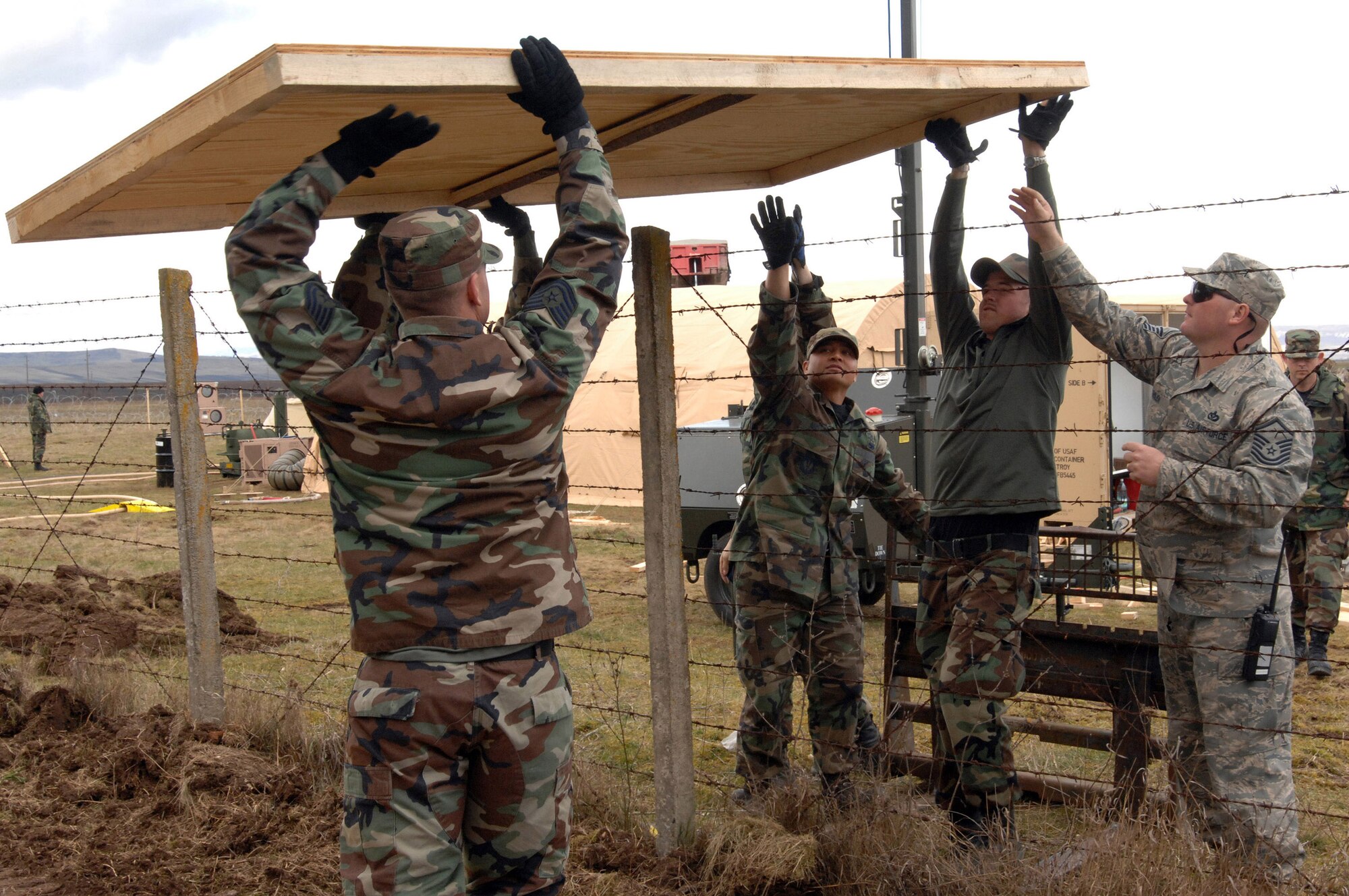 Members of the 404th Expeditionary Air Base Squadron pass a section of plywood flooring over a fence March 24 at the tent city on Campia Turzii, in Romania. The deployed civil engineering team built an entire tent city in 96 hours to support U.S. operations at the air base. The Airmen are part of a team which is augmenting NATO forces in securing the airspace around Bucharest, Romania, for the NATO Summit April 2to 4. (U.S Air Force photo/Senior Airman Teresa M. Hawkins) 