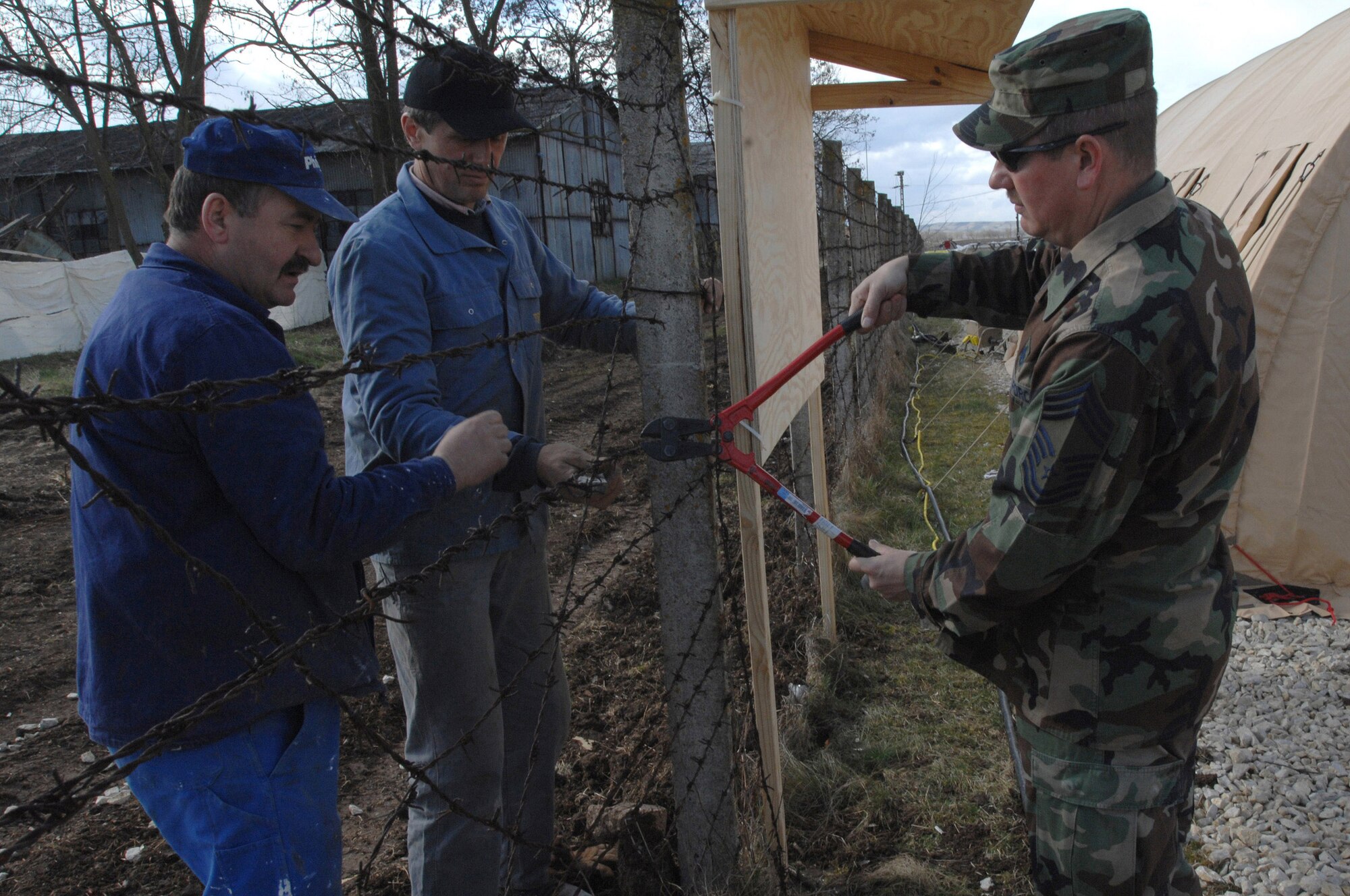 Chief Master Sgt. Terry Masters and Romanian nationals cut the fence bewteen the Romanian base and tent city March 24 at Campia Turzii, Romania. A deployed civil engineering team built an entire tent city in 96 hours to support U.S. operations at the air base. The Airmen are part of a team which is augmenting NATO forces in securing the airspace around Bucharest, Romania, for the NATO Summit April 2 to 4. Sergeant Masters is chief of the 404th Expeditionary Air Base Squadron (U.S Air Force photo/Senior Airman Teresa M. Hawkins) 