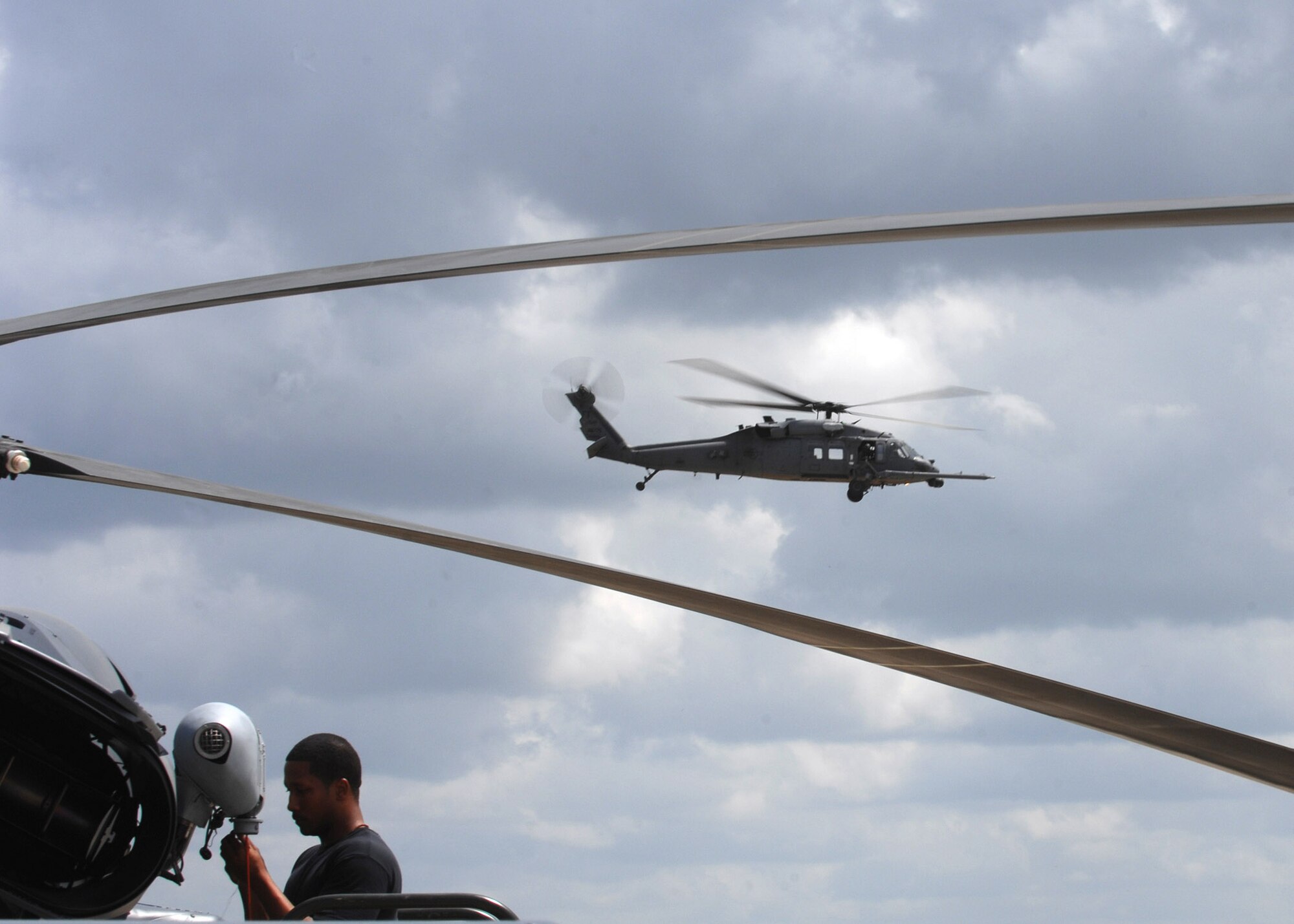 Staff Sgt. Ray Campbell installs a hoist cable squib on an HH-60G Pave Hawk at Moody Air Force Base, Ga., April 1 while another flies by in the background. The primary mission of the Pave Hawk is to conduct combat search and rescue operations.  Sergeant Campbell is an electrical and environmental technician with the 723rd Aircraft Maintenance Squadron.  (U.S. Air Force photo/Airman 1st Class Brittany Barker)