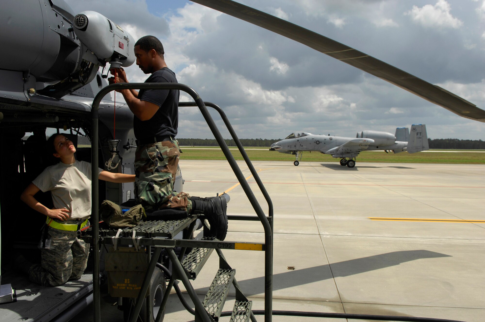 Senior Airman Stephanie Secor and Staff Sgt. Ray Campbell work on an HH-60G Pave Hawk helicopter hoist cable April 1 at Moody Air Force Base, Ga., as a Moody-assigned A-10 Thunderbolt II heads out on a training mission.  Airman Secor and Sergeant Campbell are electrical and environmental technicians with the 723rd Aircraft Maintenance Squadron.  (U.S. Air Force photo/Tech. Sgt. Parker Gyokeres)