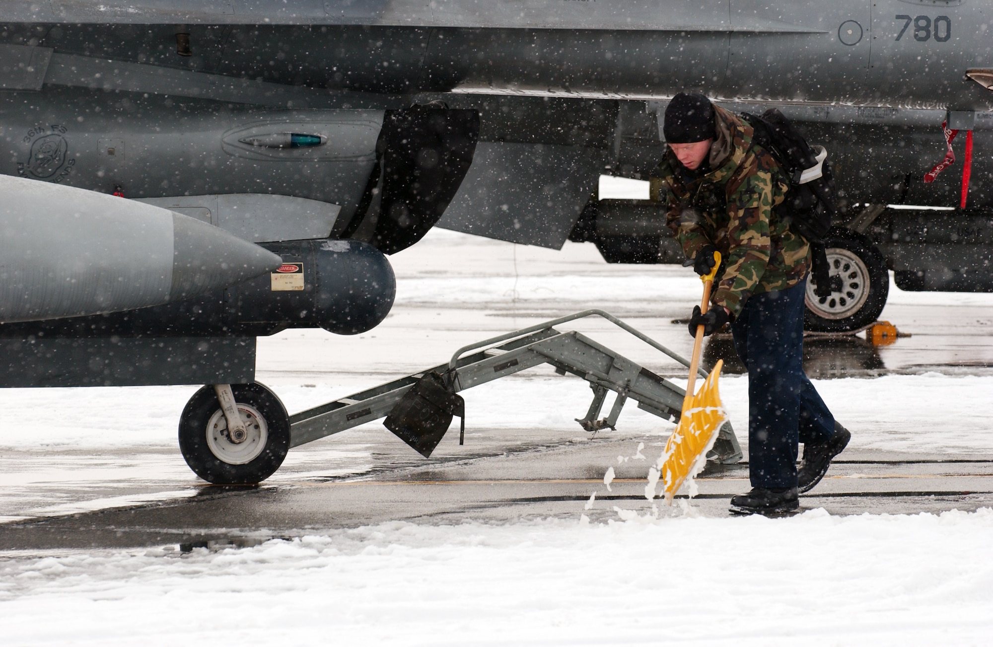 A maintainer with the 51st Aircraft Maintenance Squadron removes snow from the tarmac to clear a path to an F-16 Fighting Falcon for the first official day of Red Flag-Alaska 08-2 April 7 at Eielson Air Force Base, Alaska. Snow removal vehicles cannot clear snow withing 15 feet of an aircraft so maintainers shovel by hand. He is assigned to the Osan Air Base, Korea. (U.S. Air Force Photo/Airman 1st Class Jonathan Snyder)