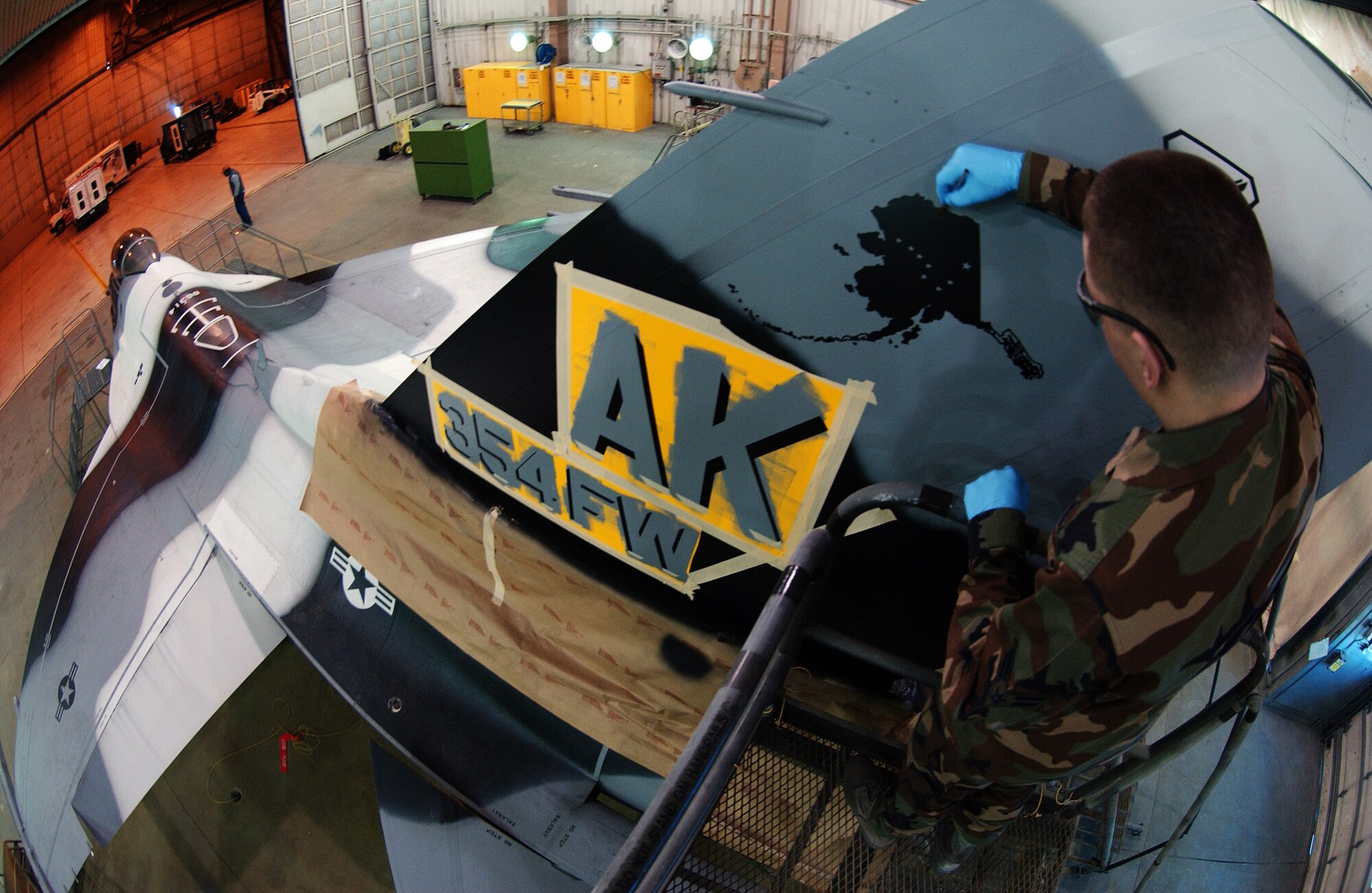 Airman 1st Class Daniel Herbert carefully applies the finishing touches to the state of Alaska stencil design on the tail March 26 at Eielson Air Force Base, Alaska. Airmen of the sheet metal shop work on stenciling the flag ship tail with unique markings setting it apart from other aggressor aircraft from the 18th Aggressor Squadron. (U.S. Air Force Photo/Airman 1st Class Jonathan Snyder)