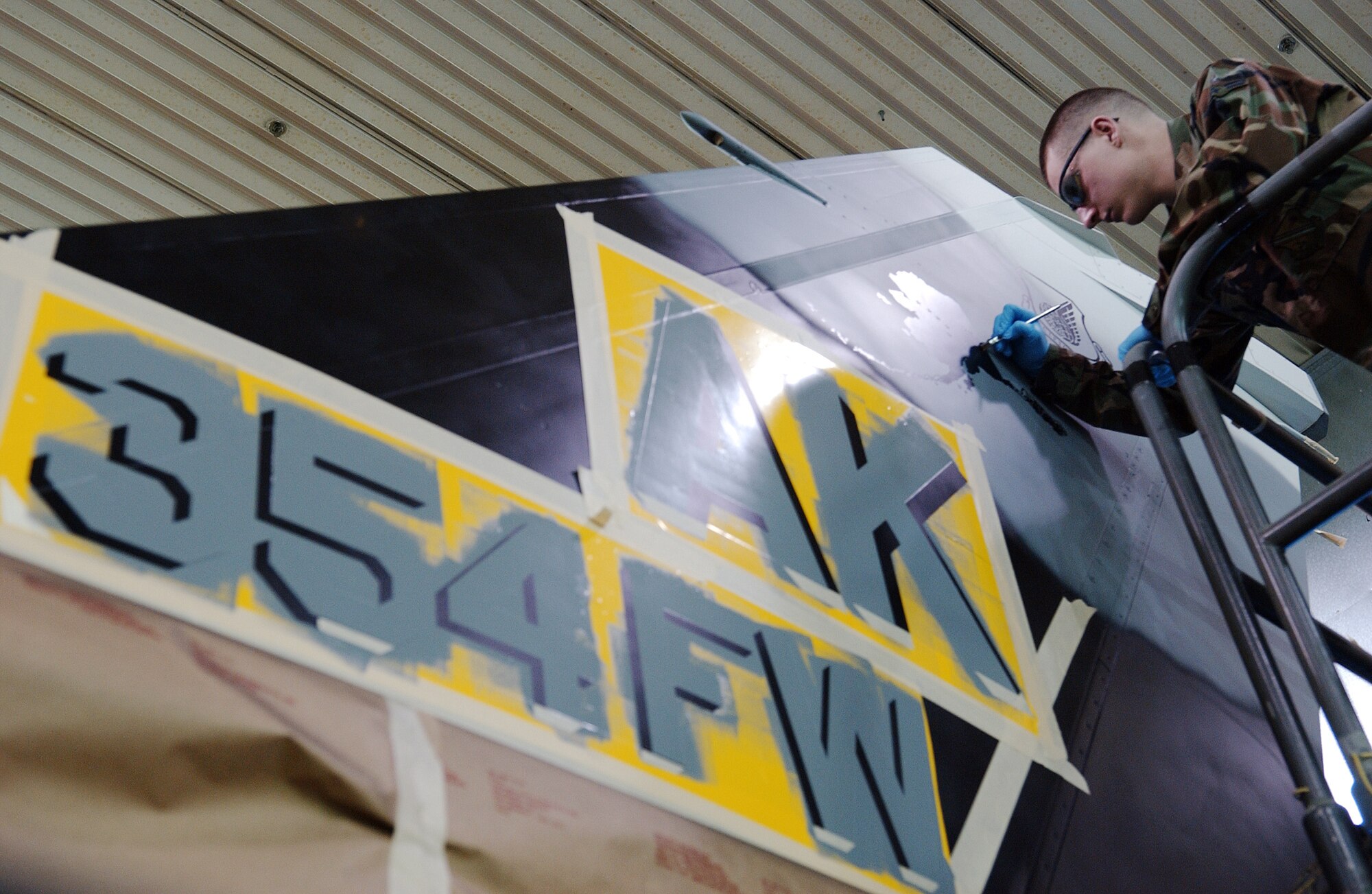 Airman 1st Class Daniel Herbert touches up the state of Alaska stencil design on the tail March 26 at Eielson Air Force Base, Alaska. Airmen of the sheet metal shop work on stenciling the flag ship tail with unique markings setting it apart from other aggressor aircraft from the 18th Aggressor Squadron. (U.S. Air Force Photo/Airman 1st Class Jonathan Snyder)