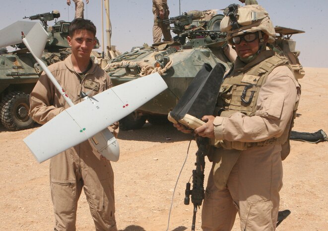 Lance Cpl. Basil M. Callahan, a welder with Charlie Company, 2nd Light Armored Reconnaissance Battalion, Regimental Combat Team 5, holds the Raven airborne unit while Cpl. Luis E. Piris-Santiago, a scout team leader and Unmanned Air Vehicle operator with Charlie Co., holds the remote control during a system demonstration April 8 in western Anbar province, Iraq.  Marines with 2nd LAR learned to fly the Raven and then got to test their skills during an operation.