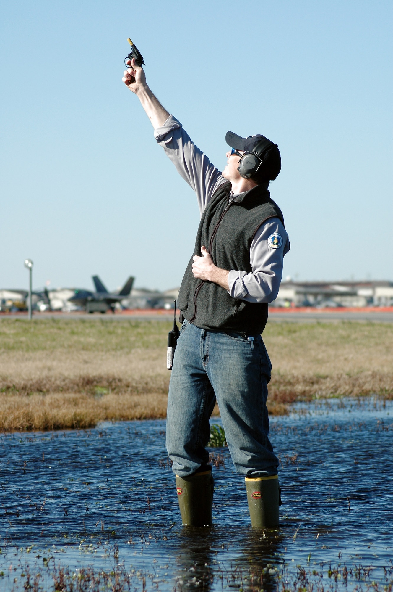 Tom Olexa shoots pyrotechnics in front of the runway here to disperse a flock of birds before a pair of F-22 Raptors (background) take off March 5 at Langley Air Force Base, Va. Wet areas around the runway attract all sorts of wildlife, including birds, which pose a hazard to launching aircraft. Mr. Olexa, a U.S. Department of Agriculture wildlife biologist,  works with the 1st Fighter Wing's Bird and Wildlife Aircraft Strike Hazard team. (U.S. Air Force photo)
