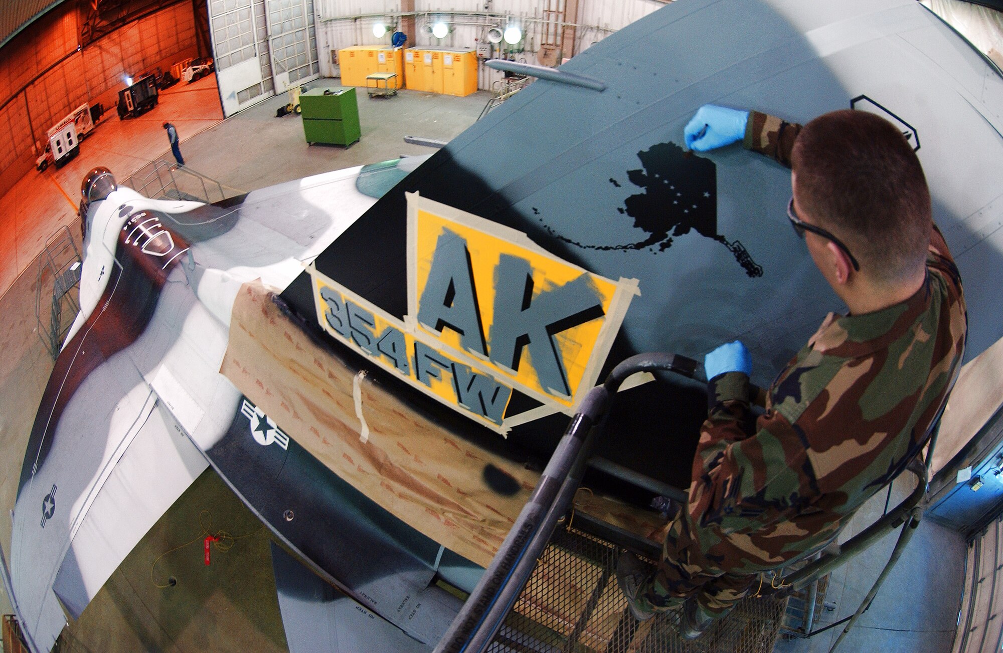 Airman 1st Class Daniel Herbert applies the finishing touches to the state of Alaska stencil design on the tail March 26 at Eielson Air Force Base, Alaska. Airmen in the sheet metal shop work on stenciling the flag ship tail with unique markings setting it apart from other aggressor aircraft from the 18th Aggressor Squadron. (U.S. Air Force Photo/Airman 1st Class Jonathan Snyder)