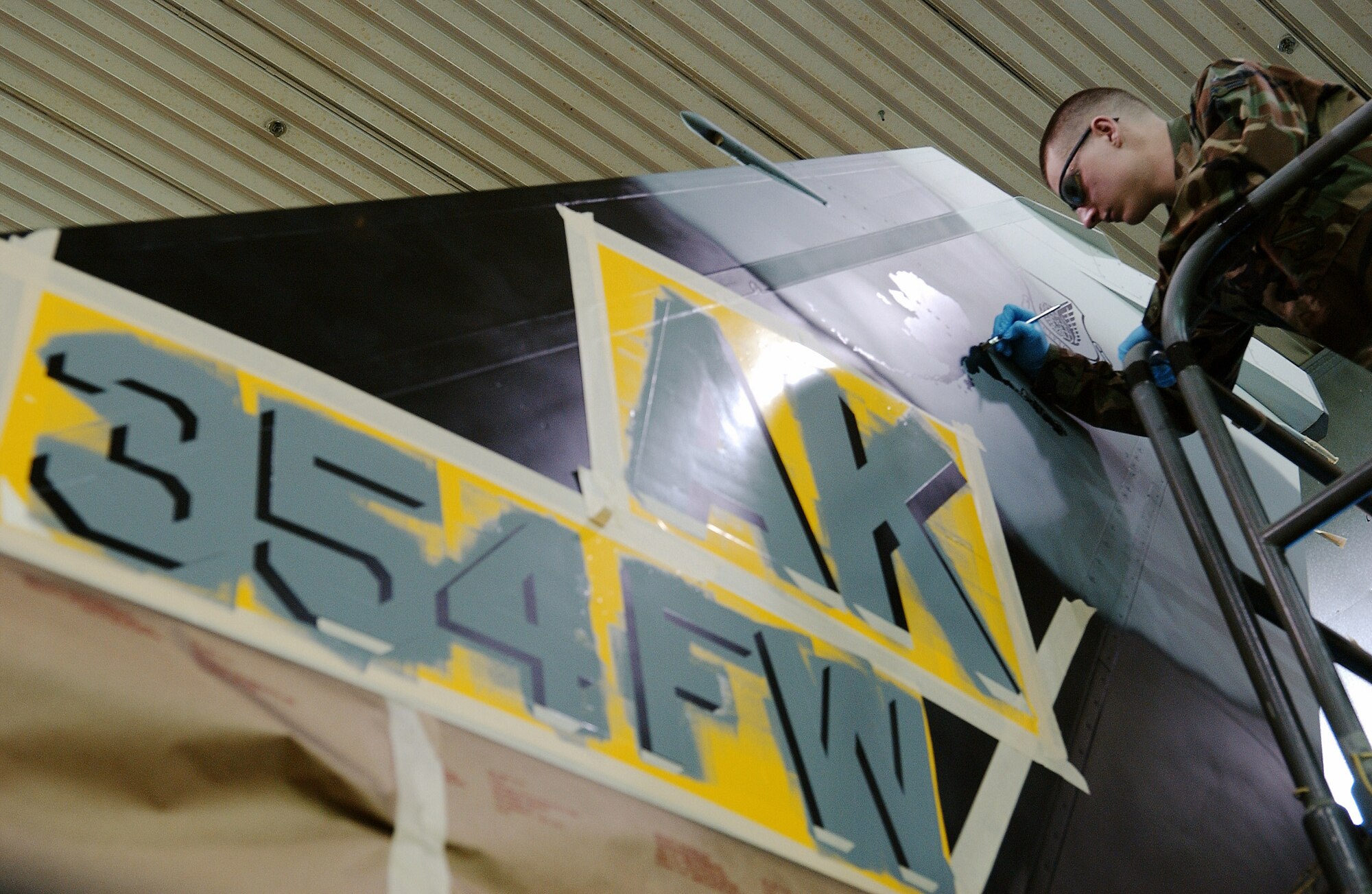 Airman 1st Class Daniel Herbert touches up the state of Alaska stencil design on the tail March 26 at Eielson Air Force Base, Alaska. Airmen in the sheet metal shop work on stenciling the flag ship tail with unique markings setting it apart from other aggressor aircraft from the 18th Aggressor Squadron. (U.S. Air Force Photo/Airman 1st Class Jonathan Snyder)