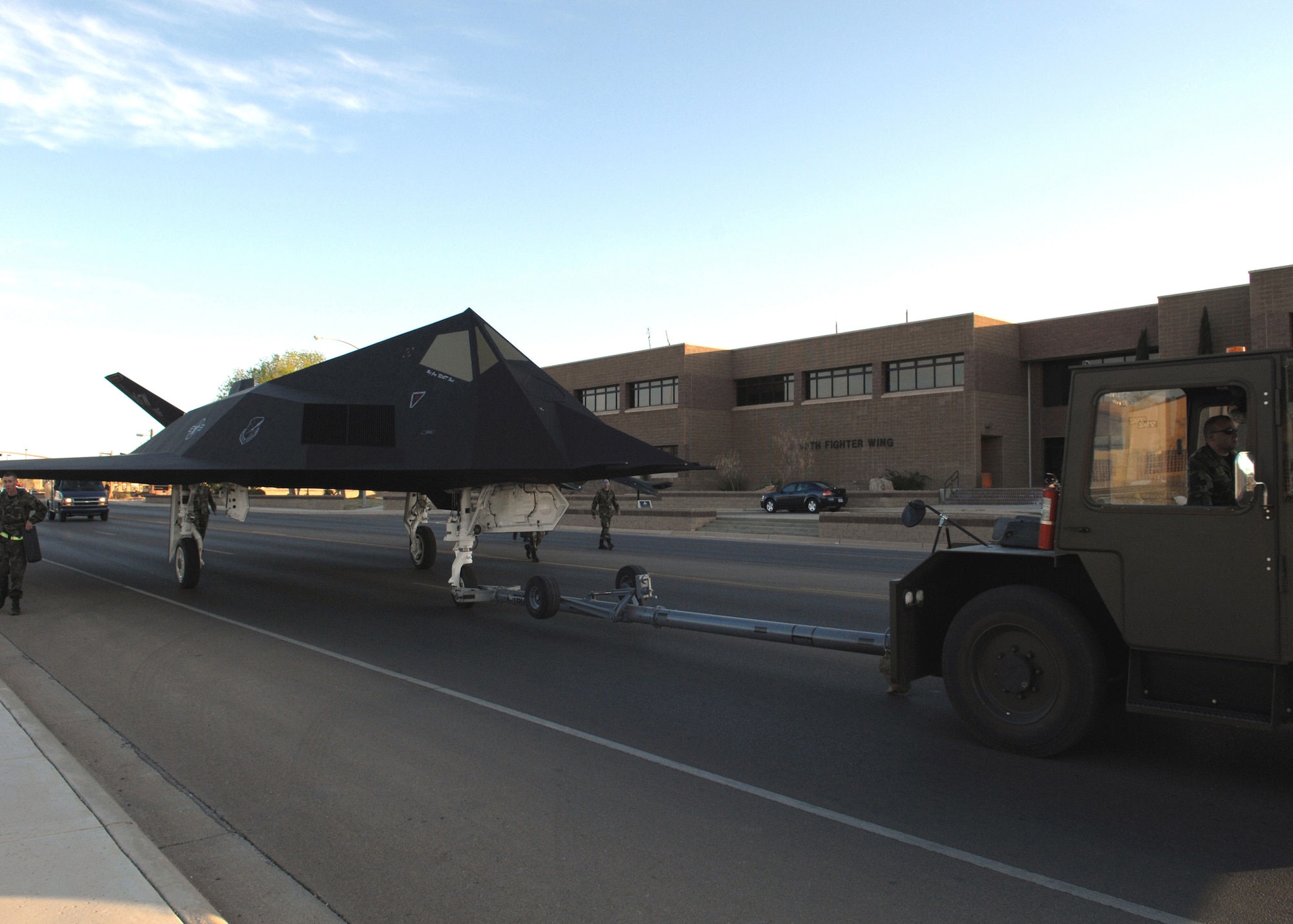 HOLLOMAN AIR FORCE BASE, N.M. -- Airmen from the 49th Maintenance Squadron escort an F-117A past the 49th Fighter Wing Headquarters to its new home in Heritage Park April 5. The personnel were performing what is called a  "chock walk" to insure the aircraft didn't become detached from the tow vehicle. (U.S. Air Force photo by Airman Sondra M. Wieseler)
