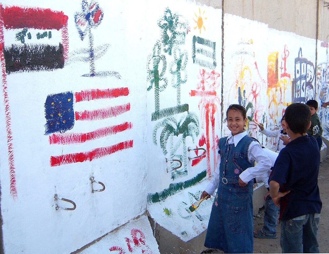 An Iraqi girl poses in front of her artwork and the Iraqi and American flags, as other children paint during a fun day celebrated at Forward Operating Base War Eagle in northern Baghdad, March 29, 2008. Children of the village next to War Eagle painted the T-walls that line their route to school. Photo by Army Capt. Walter Zurkowski, 3rd Brigade Combat Team, 4th Infantry Division, Multinational Division Baghdad