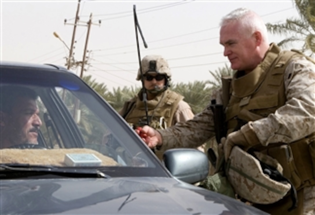 U.S. Marine Corps Col. Patrick J. Malay, commander, Regimental Combat Team 5, hands a man candy to give to his children during a vehicle check in Baghdad, Iraq, April 4, 2008. 