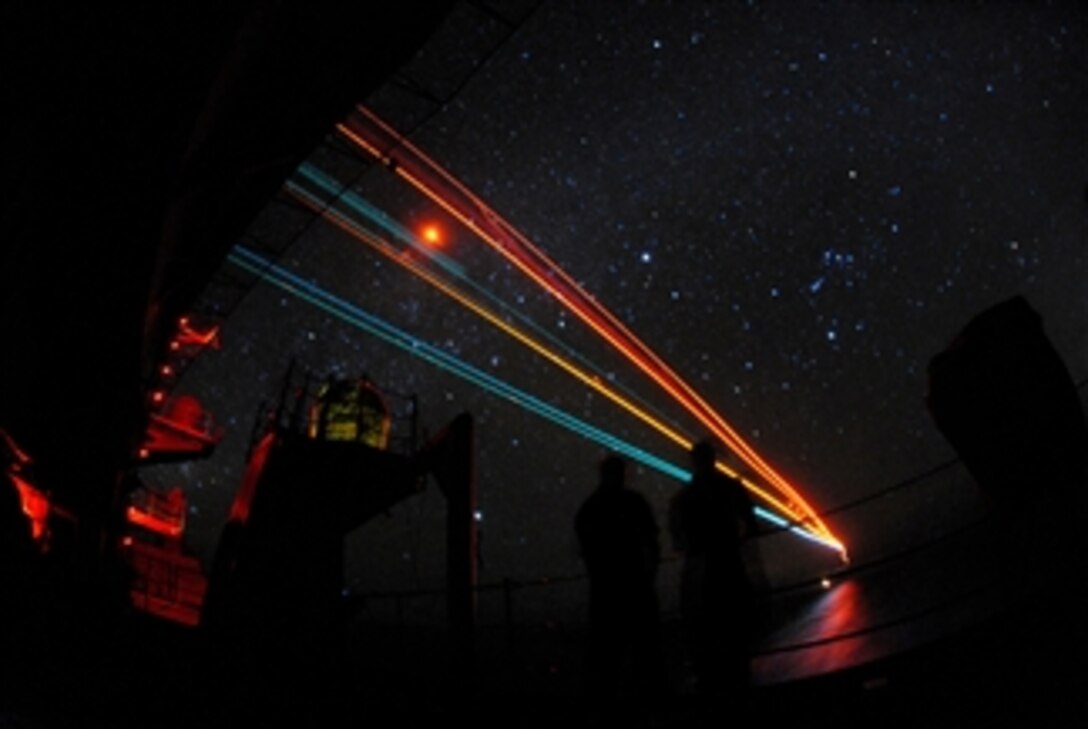 U.S. Navy sailors watch from the fantail as aircraft from Carrier Air Wing 2 streak to a night landing on the aircraft carrier USS Abraham Lincoln (CVN 72) during flight operations in the Pacific Ocean on April 7, 2008.  