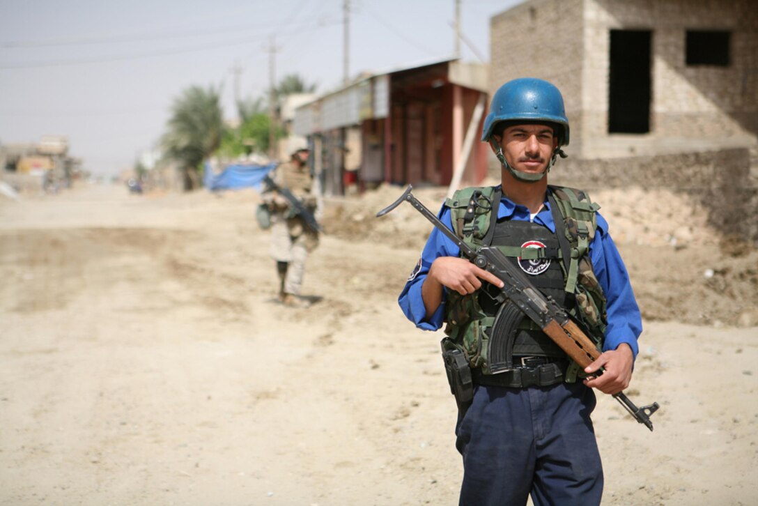 An Iraqi policeman patrols through Hit, Iraq, April 9 with a Marine following behind. Four policemen joined Marines from I Company, 3rd Battalion, 4th Marine Regiment, Regimental Combat Team 5 on a security patrol through the city. Despite the language barrier due to the Marines not having an interpreter, the patrol went smoothly. Marines used hand signals throughout the patrol, and the Iraqis were able to comprehend them.