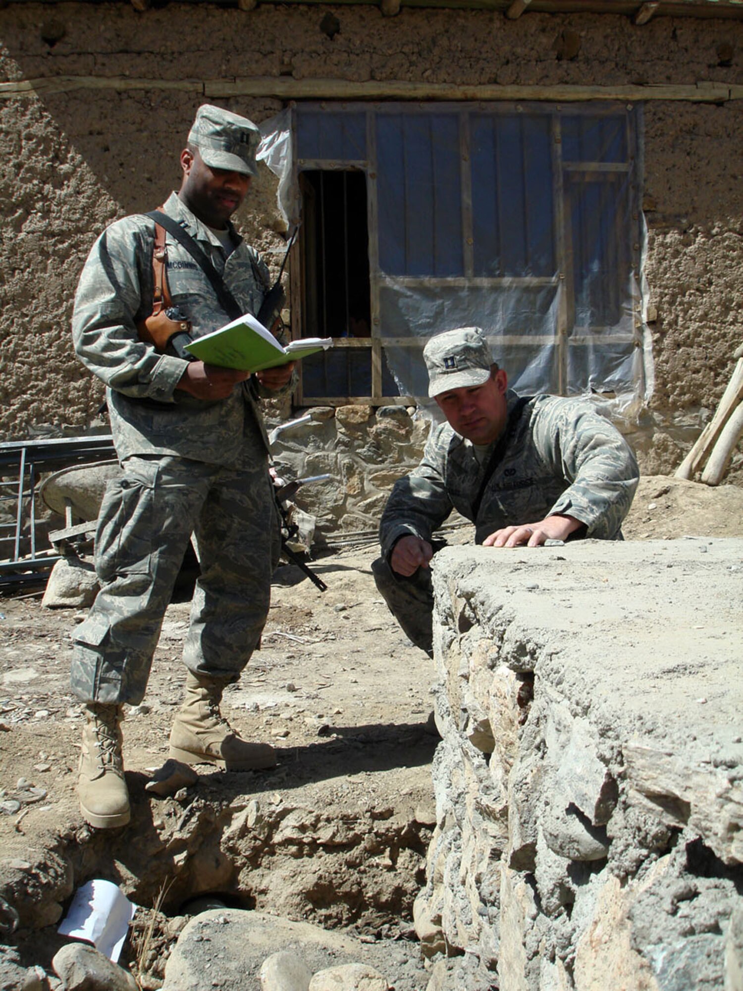Capt. Jason Aftanas takes an initial look at a foundation for a schoolbook repository and dictates information to Capt. Kenneth McGinnis at a site near the Khenj District Center April 1 in Afghanistan. The captains are Panjshir Provincial Reconstruction Team engineers. (U.S. Air Force photo/Capt. Jillian Torango)