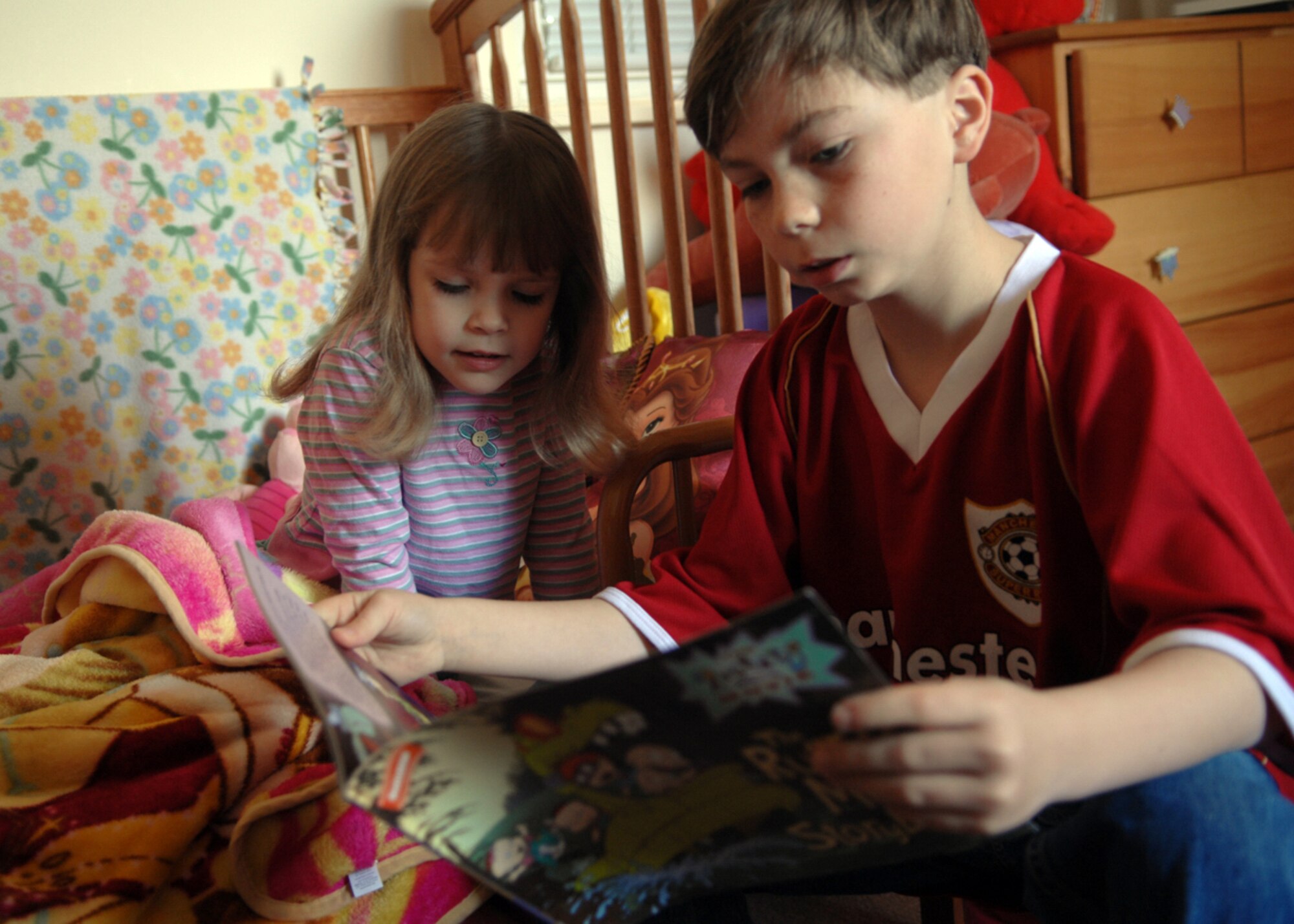 Mia Campbell (4) looks over her brother Alex's (10) shoulder as he reads her a "Rugrats" book. Mia and Alex can both earn bowling vouchers for reading together through Read-to-Bowl Program at the RAF Lakenheath Library. (U.S. Air Force photo by Tech. Sgt. Christopher Campbell)