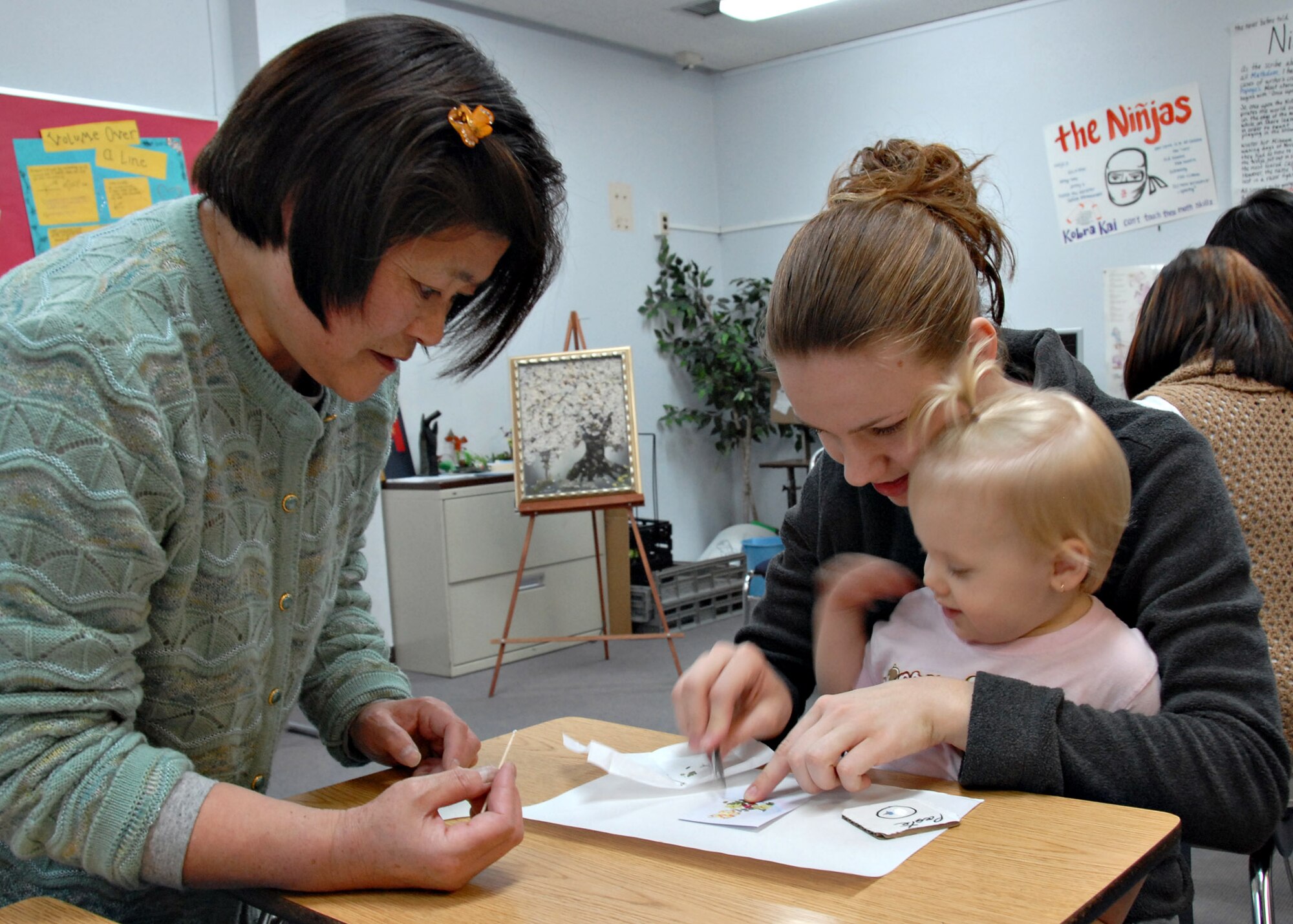 MISAWA AIR BASE, Japan – Kamee Waters and Madyon Waters, 20 months, arrange pressed flowers on a picture with the help of a Japanese artisan during Japan Day here April 5, 2008. The pressed flower picture was added to a seashell for the Americans to take home as a memento from the cultural day. (U.S. Air Force photo by Staff Sgt. Rachel Martinez)